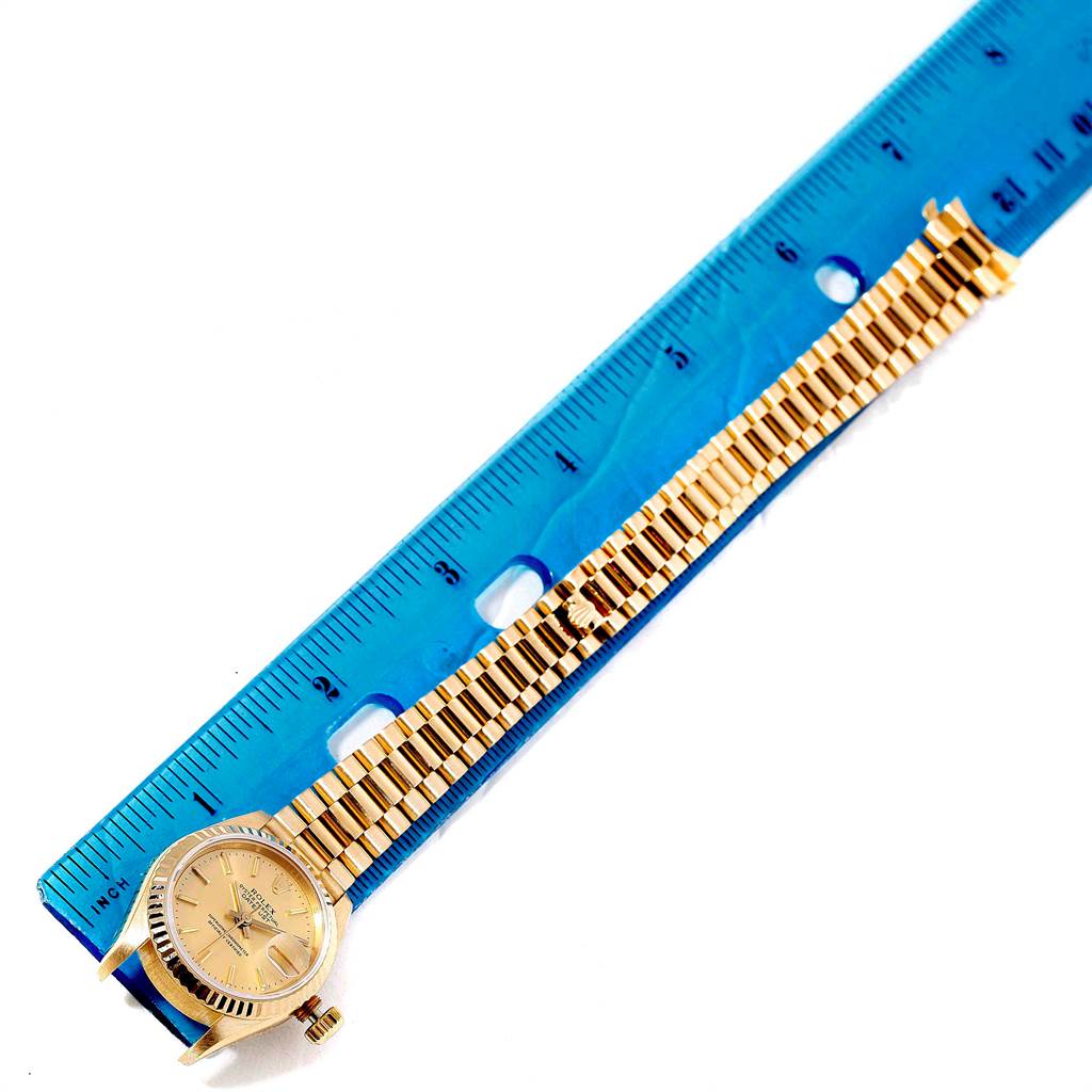 This image shows the Rolex President 69178 Women
s Yellow Gold Champagne Dial 69178 Women
s Yellow Gold Champagne Dial watch laid flat next to a blue ruler, showcasing its face and full gold band.