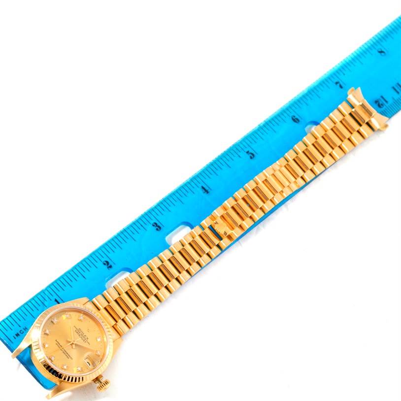 The image shows a top-down view of a Rolex President 68278 Women's Yellow Gold Champagne Dial 68278 Women's Yellow Gold Champagne Dial watch with a gold band, placed next to a blue ruler.