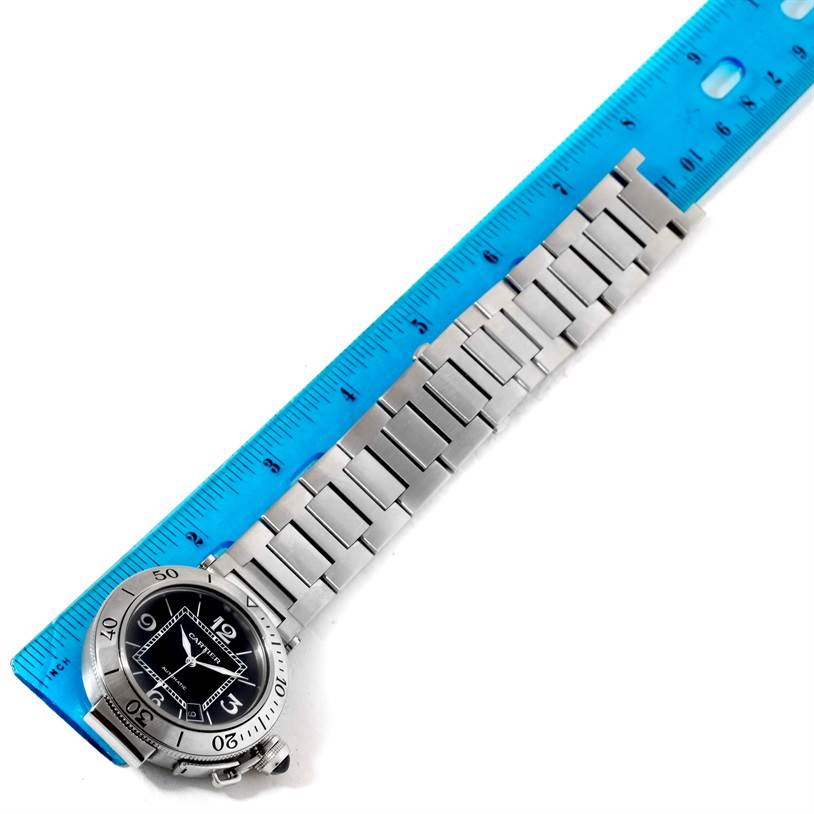 The image shows the Cartier Pasha W31077M7 Men's Stainless Steel Black Dial W31077M7 Men's Stainless Steel Black Dial watch face and bracelet from an overhead angle, placed next to a blue ruler for scale.