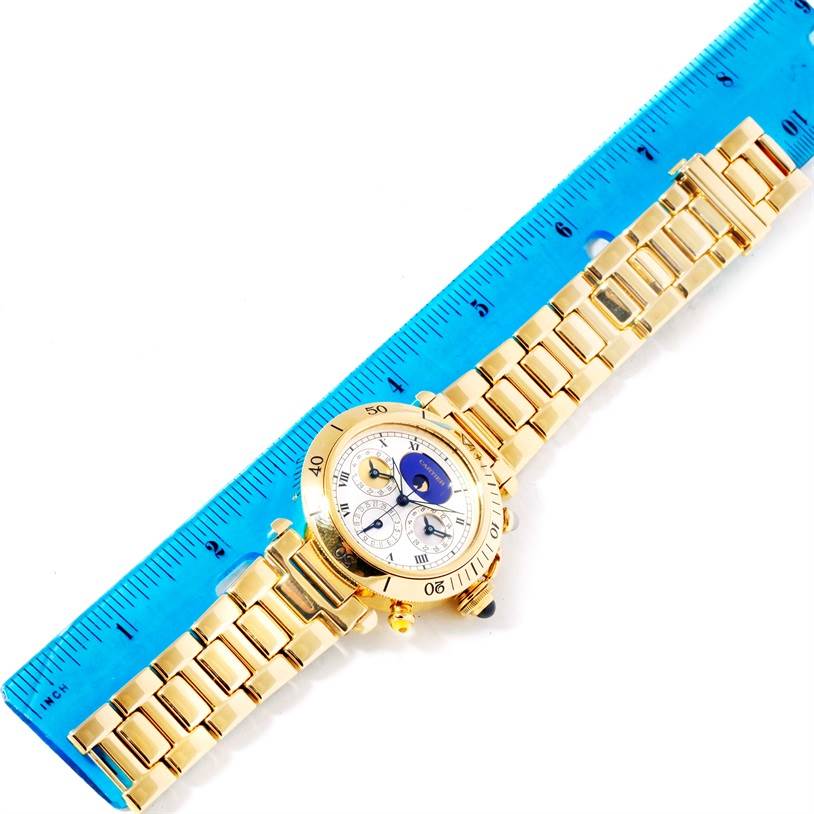 The Cartier Pasha M205025 Men's Yellow Gold Silver Dial M205025 Men's Yellow Gold Silver Dial watch is shown from a top-down angle with its entire band and face visible next to a blue ruler.