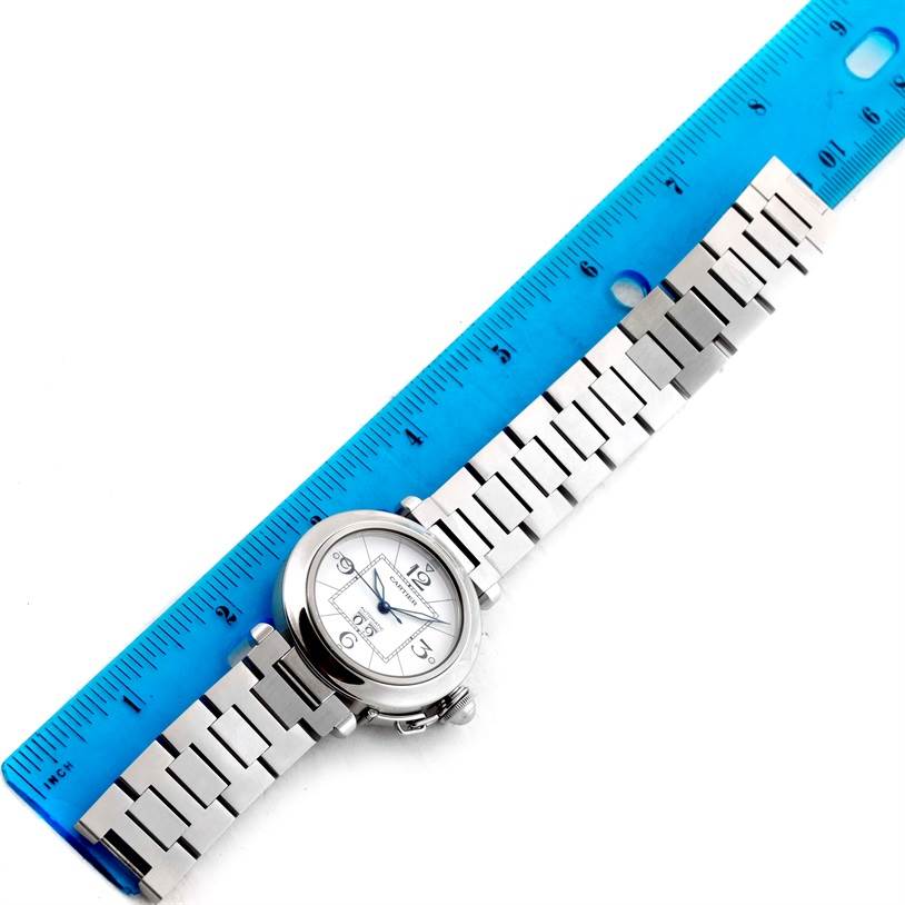The Cartier Pasha W31055M7 Men
s Stainless Steel White Dial W31055M7 Men
s Stainless Steel White Dial watch is shown from a top view with its metal band laid straight alongside a blue ruler.