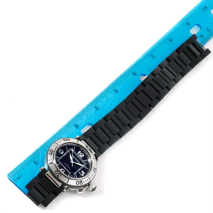 The Cartier Pasha W31077U2 Men
s Stainless Steel Black Dial W31077U2 Men
s Stainless Steel Black Dial watch is shown from a top-down angle next to a blue ruler, displaying its face and black strap.