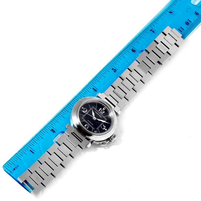 The image shows an overhead view of a Cartier Pasha W31076M7 Stainless Steel Black Dial W31076M7 Stainless Steel Black Dial watch placed next to a blue ruler, highlighting its dial and bracelet.