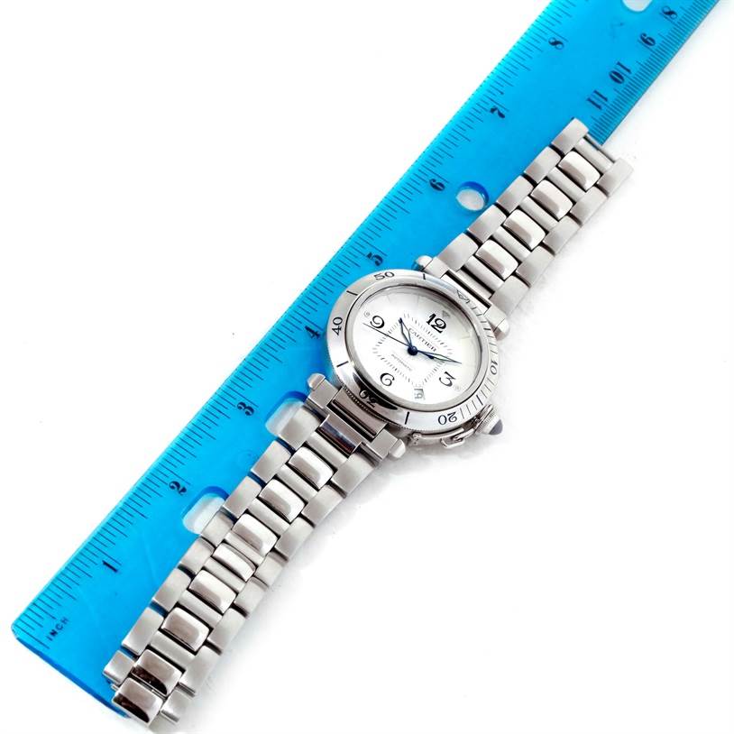 The image shows a top-down view of a Cartier Pasha W3103155 Men
s Stainless Steel Silver Dial W3103155 Men
s Stainless Steel Silver Dial watch with a stainless steel band and face, alongside a blue ruler for scale.