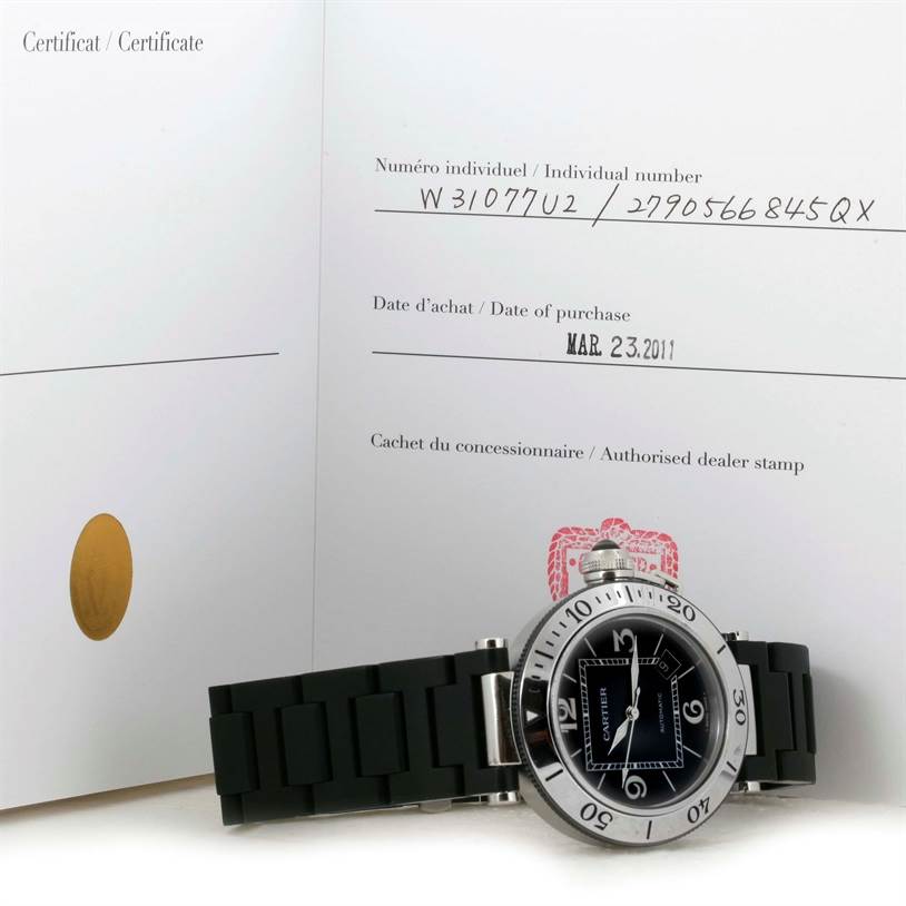 The Cartier Pasha W31077U2 Men's Stainless Steel Black Dial W31077U2 Men's Stainless Steel Black Dial watch is shown from a front angle, lying flat on its strap with documentation visible in the background.