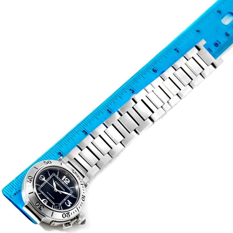 This image shows the face and stainless steel bracelet of the Cartier Pasha W31077M7 Men
s Stainless Steel Black Dial W31077M7 Men
s Stainless Steel Black Dial watch laid next to a blue ruler.