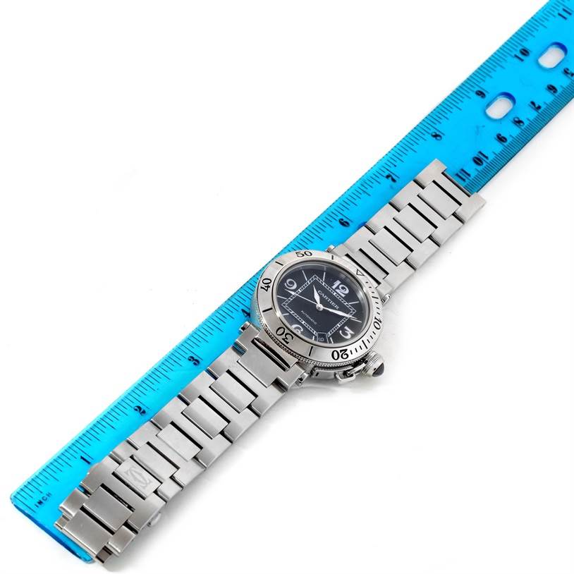 The Cartier Pasha W31077M7 Men's Stainless Steel Black Dial W31077M7 Men's Stainless Steel Black Dial watch is shown lying flat beside a blue ruler, displaying its face, bezel, and metal bracelet.