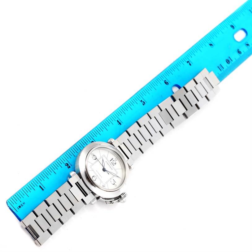 The Cartier Pasha W31074M7 Women's Stainless Steel White Dial W31074M7 Women's Stainless Steel White Dial watch is shown laying flat next to a blue ruler, displaying its face and metal strap.
