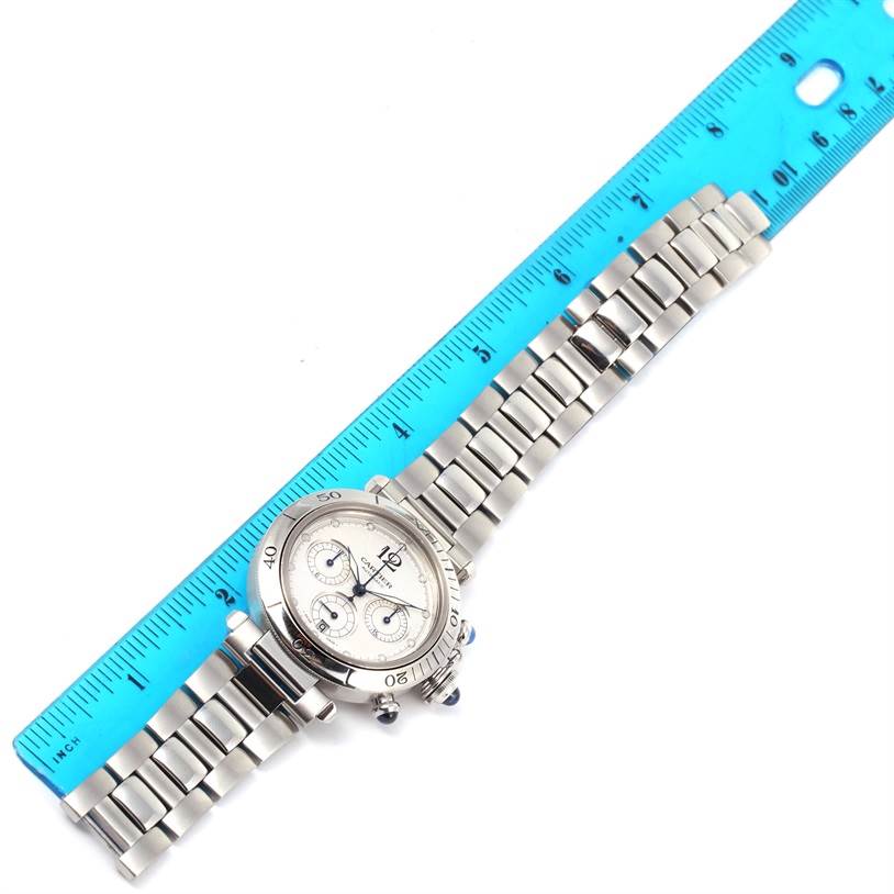 The Cartier Pasha W31030H3 Men's Silver Dial W31030H3 Men's Silver Dial watch is shown laid out flat alongside a blue ruler, displaying both the face and the band.