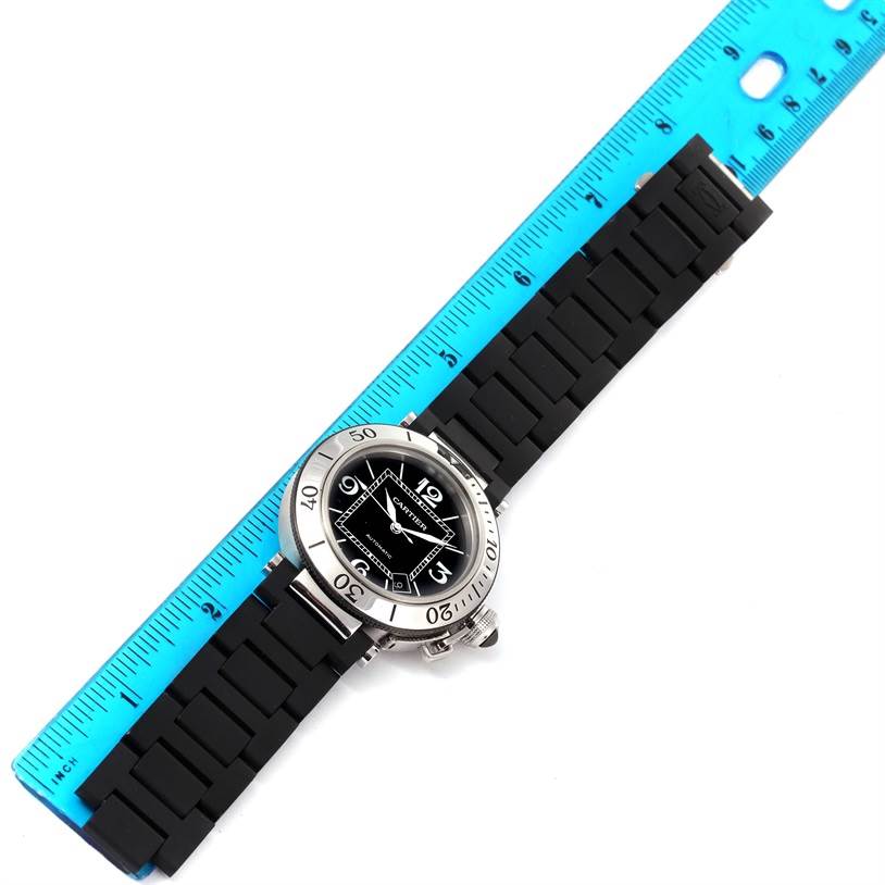 The image shows a top-down view of the Cartier Pasha W31077U2 Men's Stainless Steel Black Dial W31077U2 Men's Stainless Steel Black Dial model watch with a black strap and a blue ruler beside it for scale.