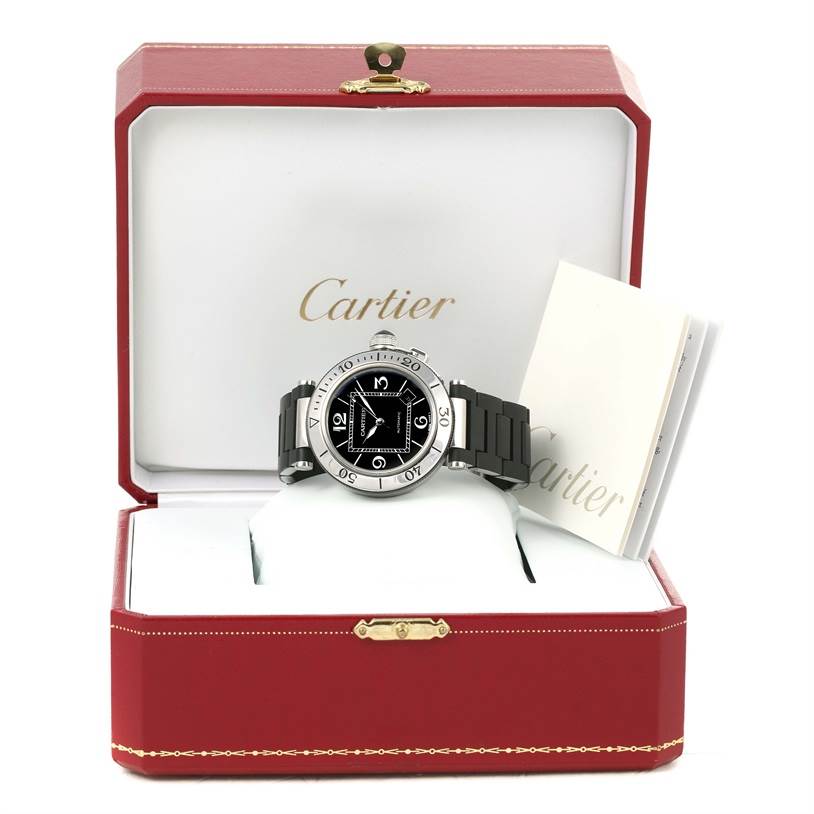 The Cartier Pasha W31077U2 Men's Stainless Steel Black Dial W31077U2 Men's Stainless Steel Black Dial watch is shown from the front, placed in an open box with some documentation beside it.