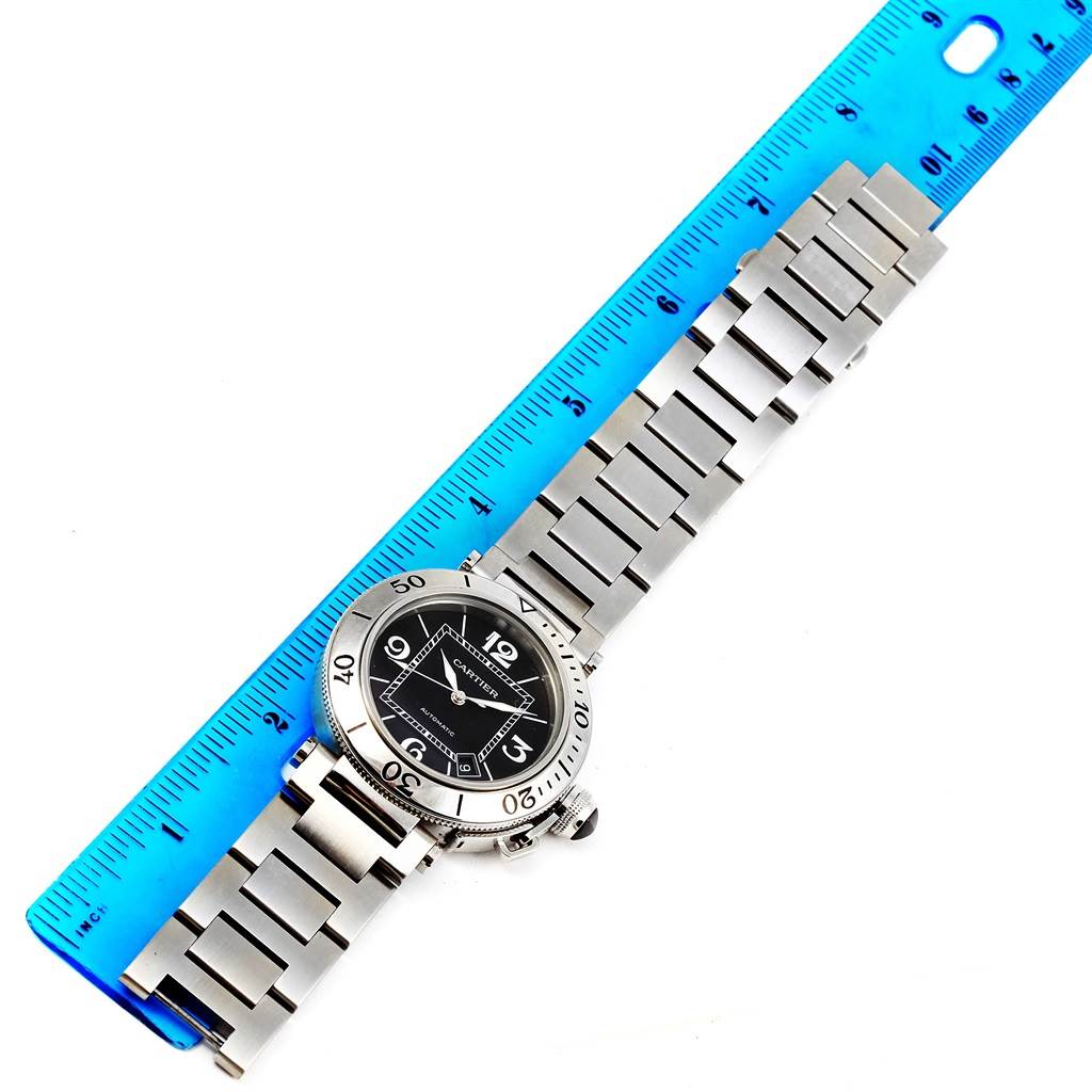 The Cartier Pasha W31077M7 Men's Stainless Steel Black Dial W31077M7 Men's Stainless Steel Black Dial watch is shown flat from above, featuring the dial and stainless steel bracelet, next to a blue ruler.