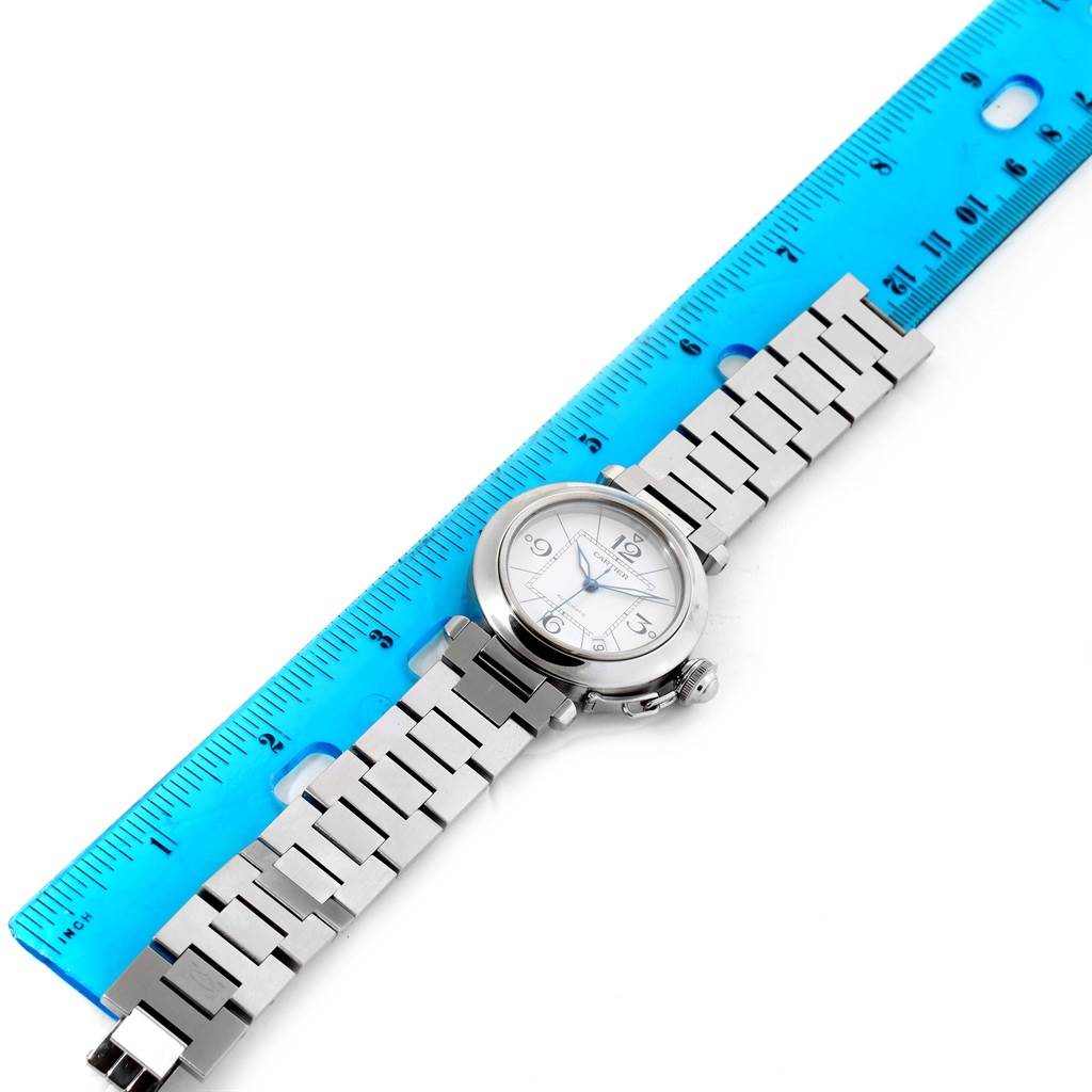 The Cartier Pasha W31074M7 Stainless Steel White Dial W31074M7 Stainless Steel White Dial watch is displayed flat with its metal bracelet fully extended alongside a blue ruler for size reference.