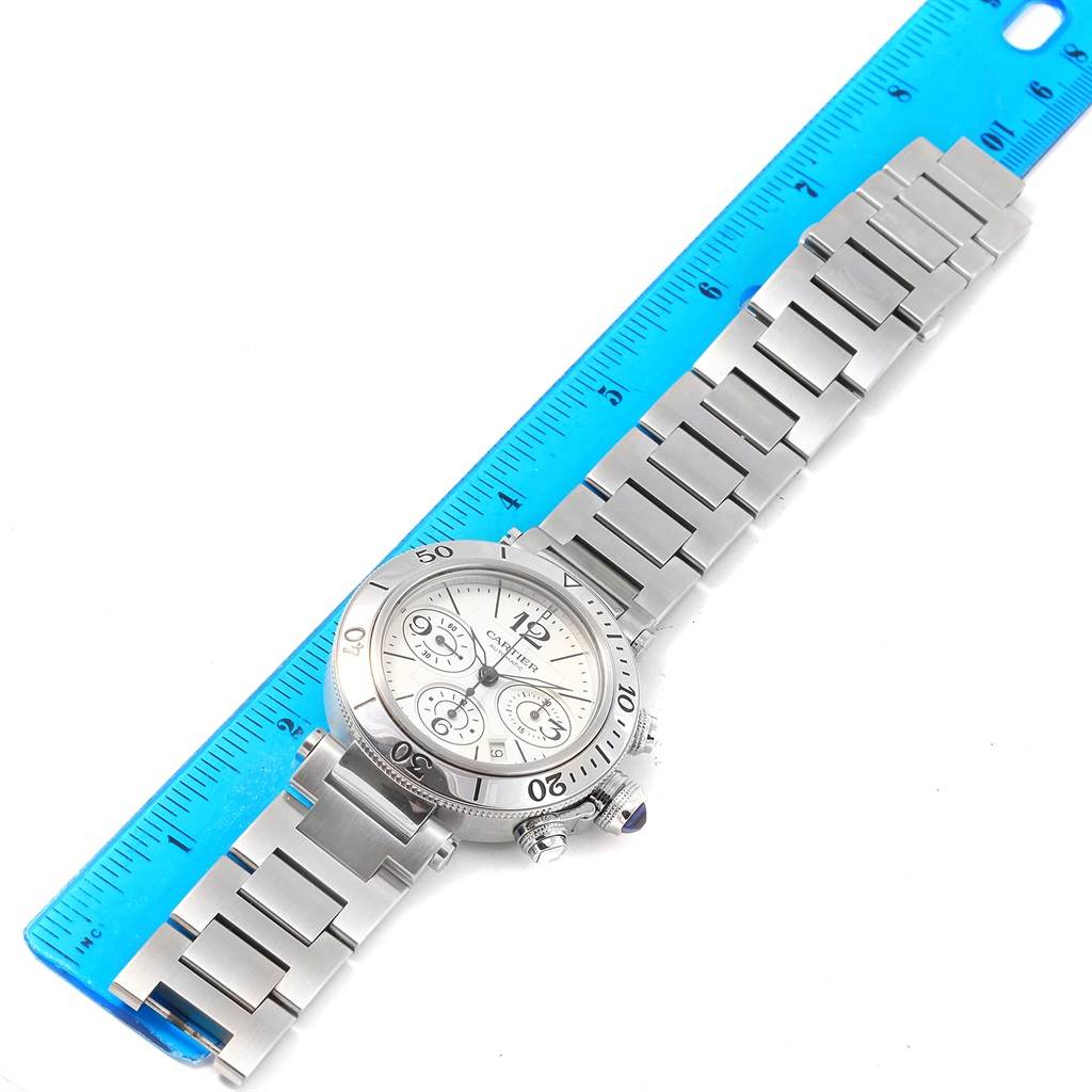 The Cartier Pasha W31089M7 Men's Stainless Steel Silver Dial W31089M7 Men's Stainless Steel Silver Dial watch is shown from a top-down angle, laid flat beside a blue ruler for scale.