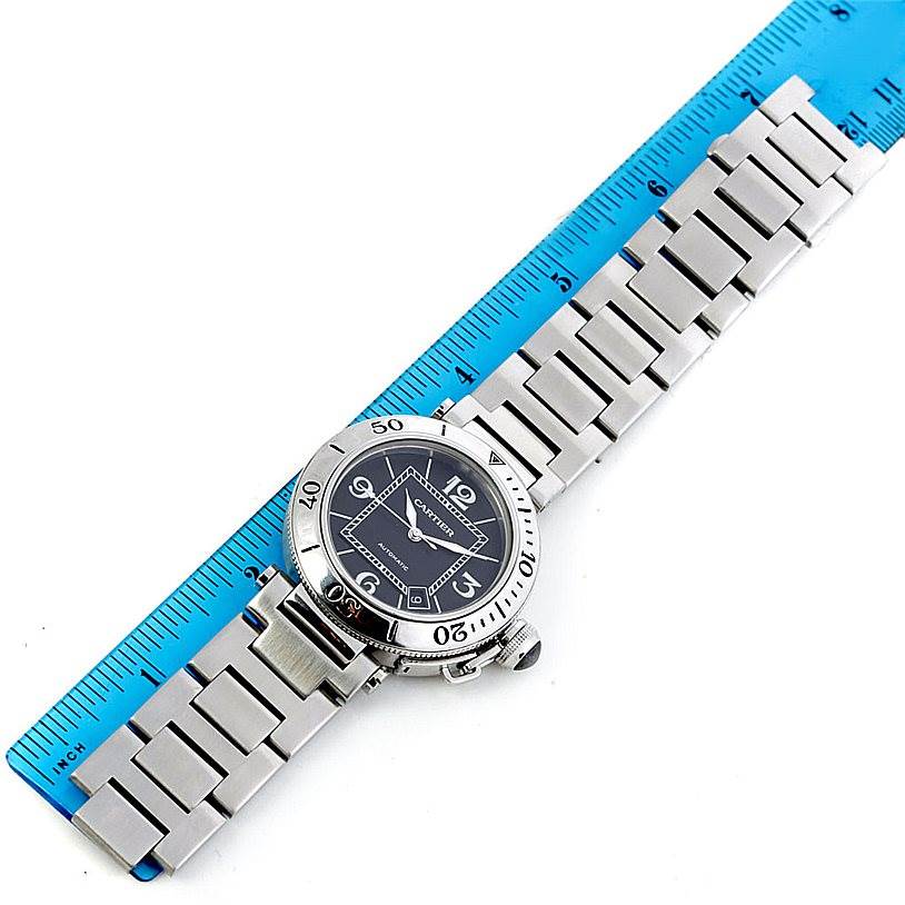 The Cartier Pasha W31077M7 Men's Stainless Steel Black Dial W31077M7 Men's Stainless Steel Black Dial watch is shown from a top-down angle, displaying its face, bezel, bracelet, and a portion of the clasp alongside a ruler for scale.