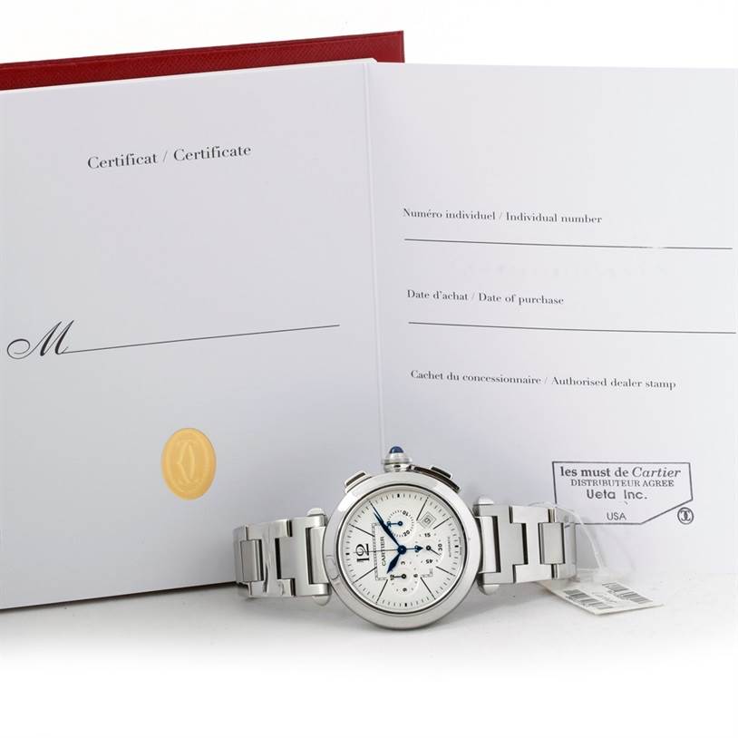 The image shows a Cartier Pasha W31085M7 Men's Stainless Steel Silver Dial W31085M7 Men's Stainless Steel Silver Dial model watch laid flat in front of its open certificate booklet.