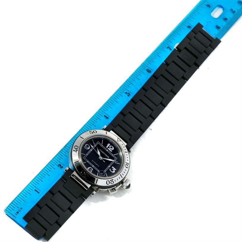 The Cartier Pasha W31077U2 Men
s Stainless Steel Black Dial W31077U2 Men
s Stainless Steel Black Dial watch is shown from a top-down angle, displaying the face and full rubber strap next to a ruler for size reference.