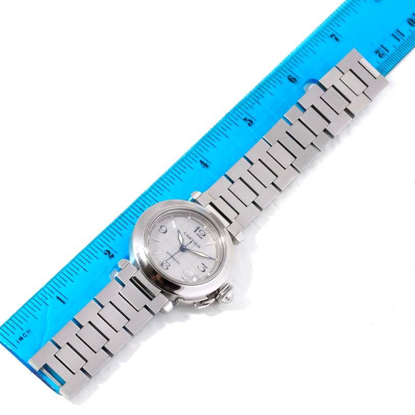 The image shows a Cartier Pasha W31023M7 Men's Stainless Steel Grey Dial W31023M7 Men's Stainless Steel Grey Dial model watch laid flat beside a blue ruler, displaying its face and metal bracelet band.