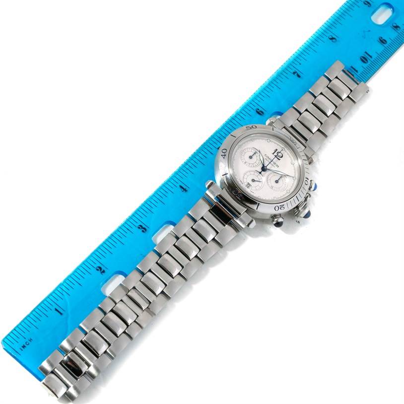 The image shows a Cartier Pasha W31030H3 Men
s Stainless Steel Silver Dial W31030H3 Men
s Stainless Steel Silver Dial watch placed next to a blue ruler, displaying the watch face and metal bracelet.