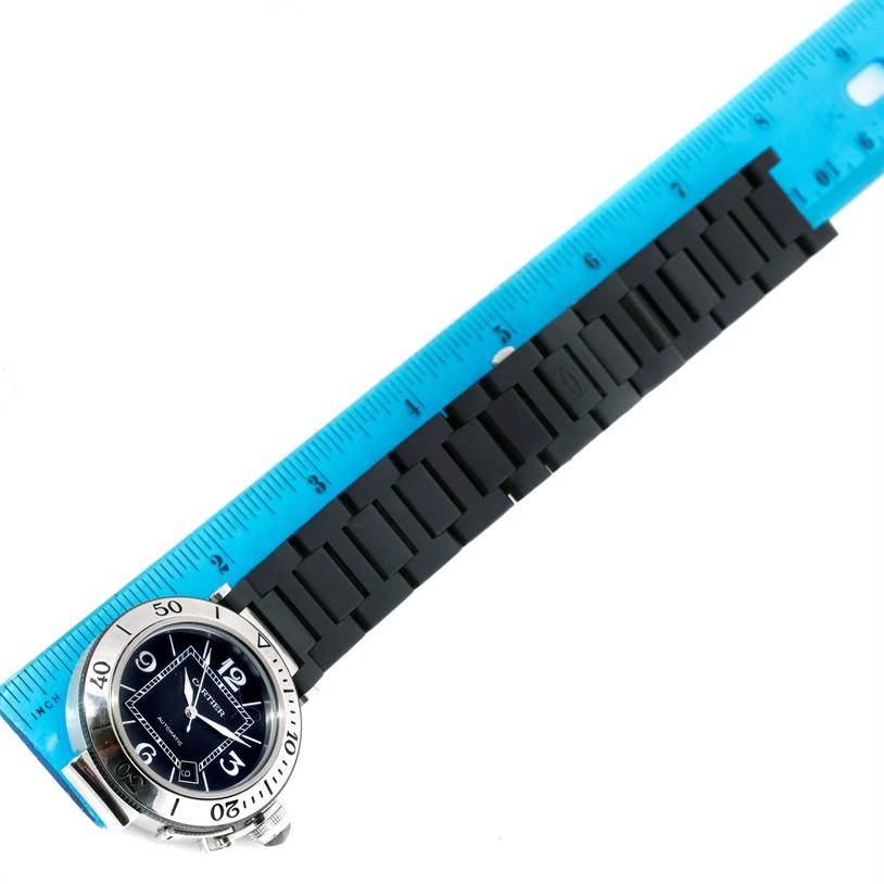 The Cartier Pasha W31077U2 Men's Stainless Steel Black Dial W31077U2 Men's Stainless Steel Black Dial watch is shown from above, displaying the face, bezel, and part of the rubber strap next to a ruler for scale.