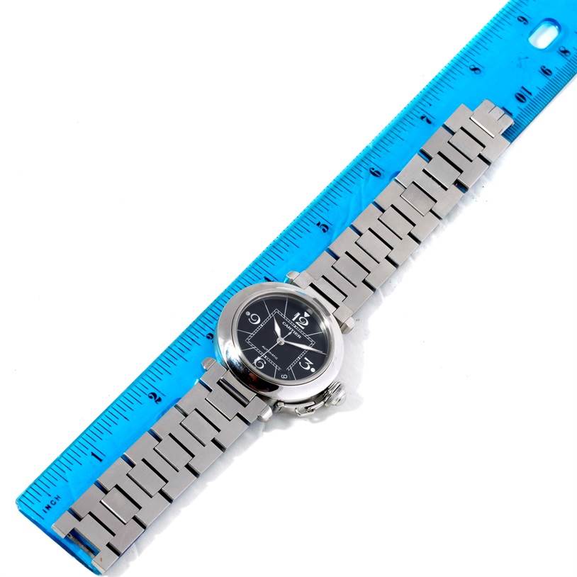 The image shows a top-down view of the Cartier Pasha W31076M7 Women's Stainless Steel Black Dial W31076M7 Women's Stainless Steel Black Dial watch, placed next to a blue ruler displaying its stainless steel bracelet and face.