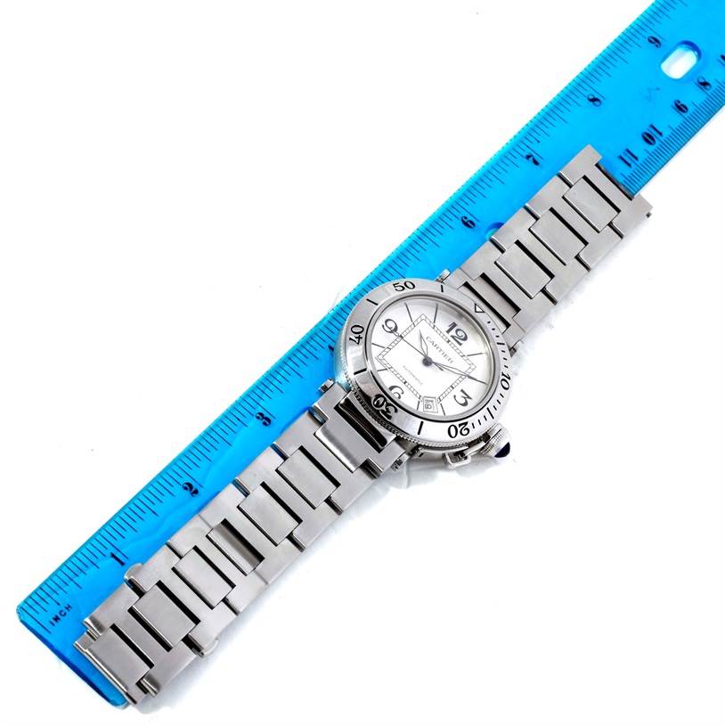 The Cartier Pasha W31080M7 Men
s Stainless Steel Silver Dial W31080M7 Men
s Stainless Steel Silver Dial watch is shown from a top-down angle with its bracelet extended alongside a blue ruler for scale.