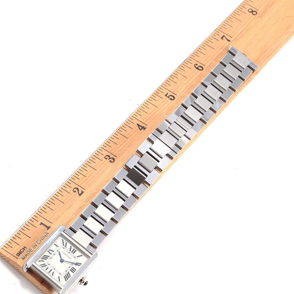 The image shows a top view of a Cartier Tank Solo W5200013 Women's Stainless Steel Silver Dial W5200013 Women's Stainless Steel Silver Dial watch alongside a wooden ruler, highlighting the watch's face and metal strap.