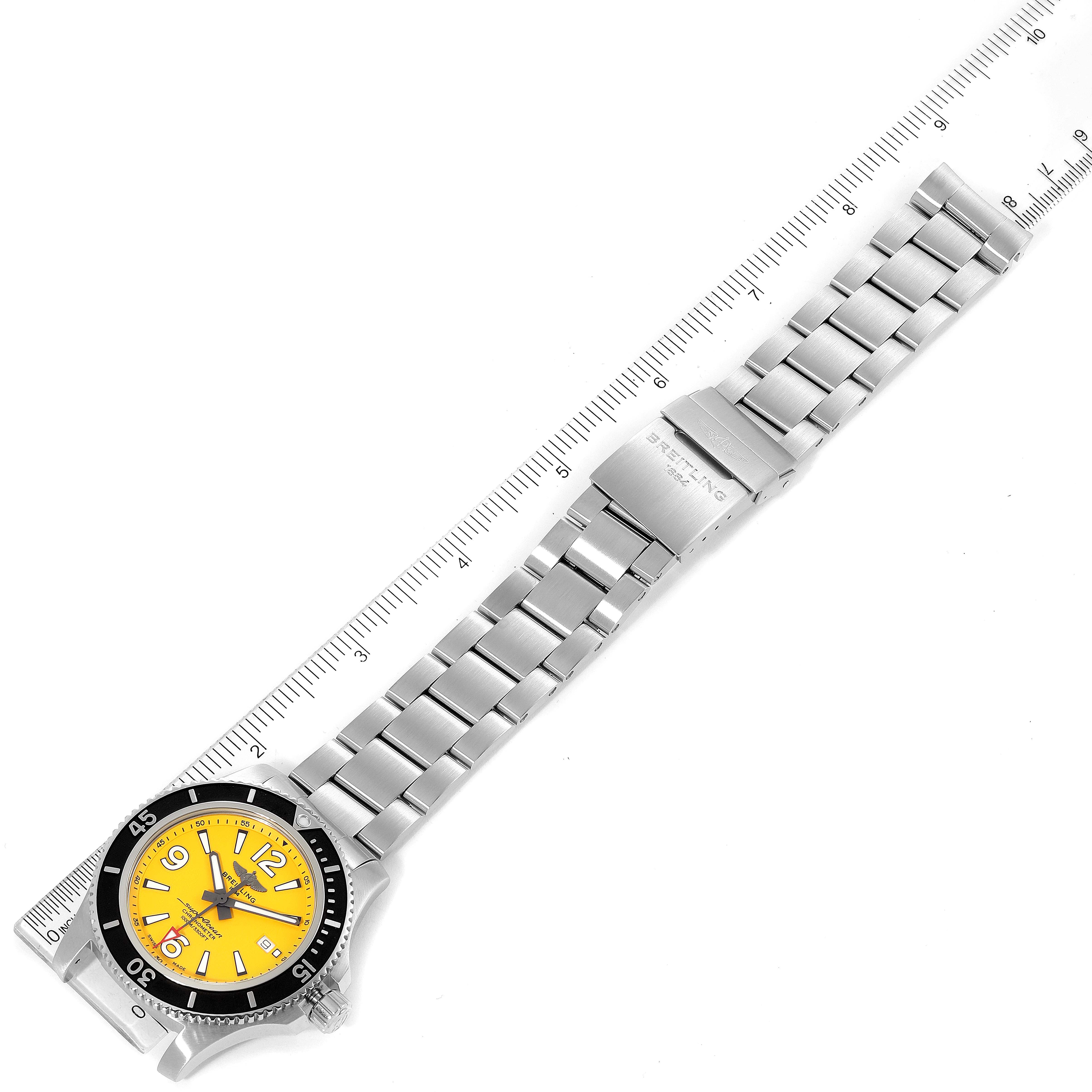 The image shows the top view of a Breitling Superocean A17367021I1A1 Men's Stainless Steel Yellow Dial A17367021I1A1 Men's Stainless Steel Yellow Dial watch with a yellow dial and metal bracelet next to a ruler.
