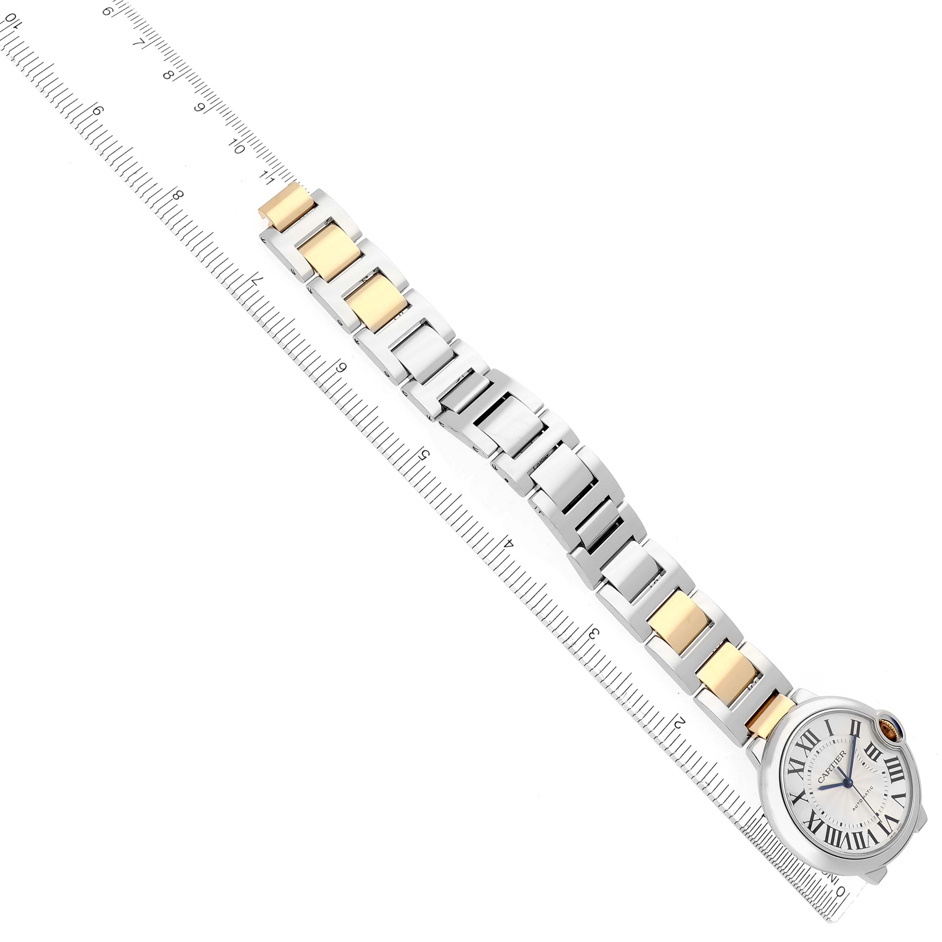 The Ballon Bleu by Cartier is shown from above, highlighting its face and two-tone metal bracelet alongside a ruler.