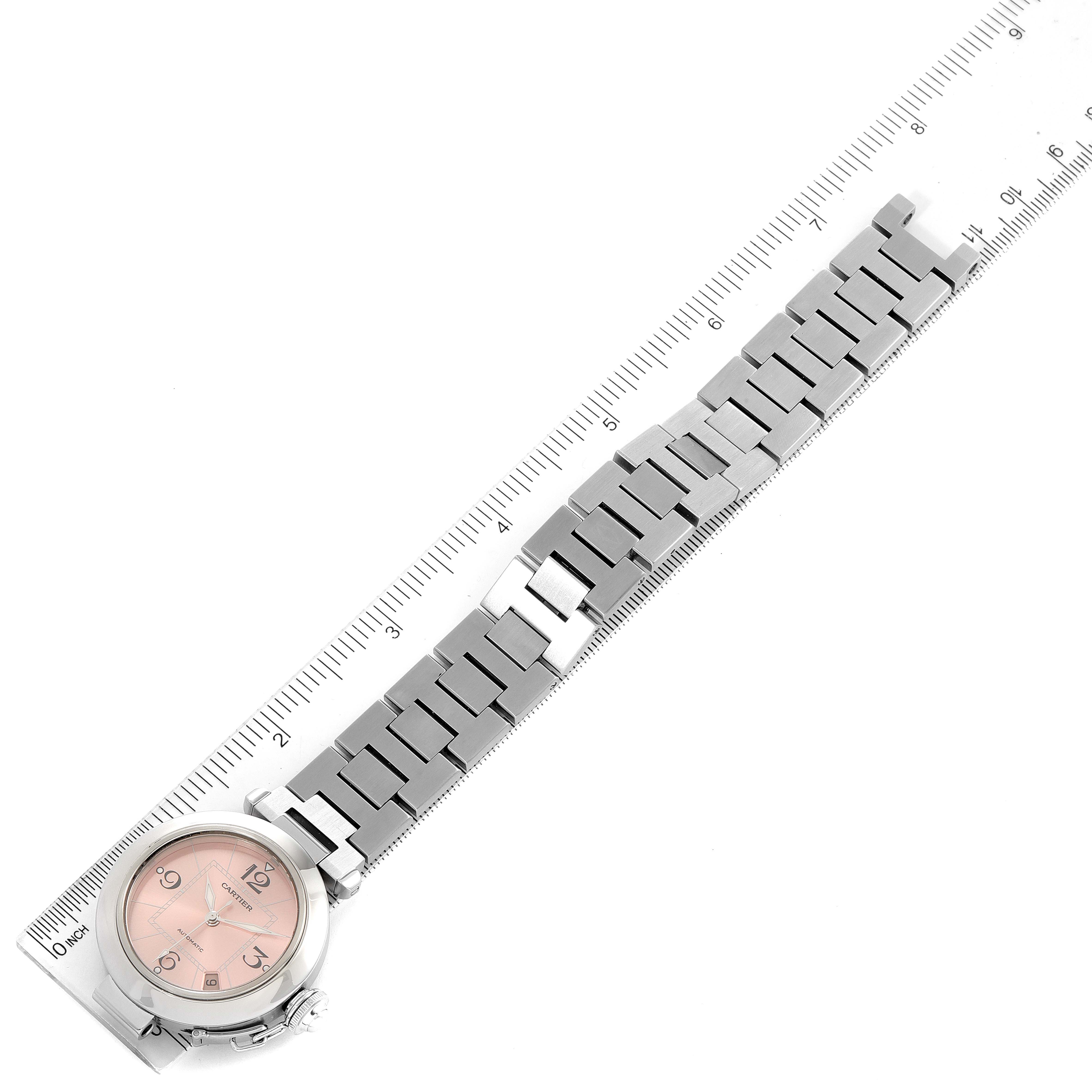 The image shows a Cartier Pasha W31075M7 Women's Stainless Steel Pink Dial W31075M7 Women's Stainless Steel Pink Dial model watch laid flat against a ruler, highlighting the watch's face and metal bracelet.