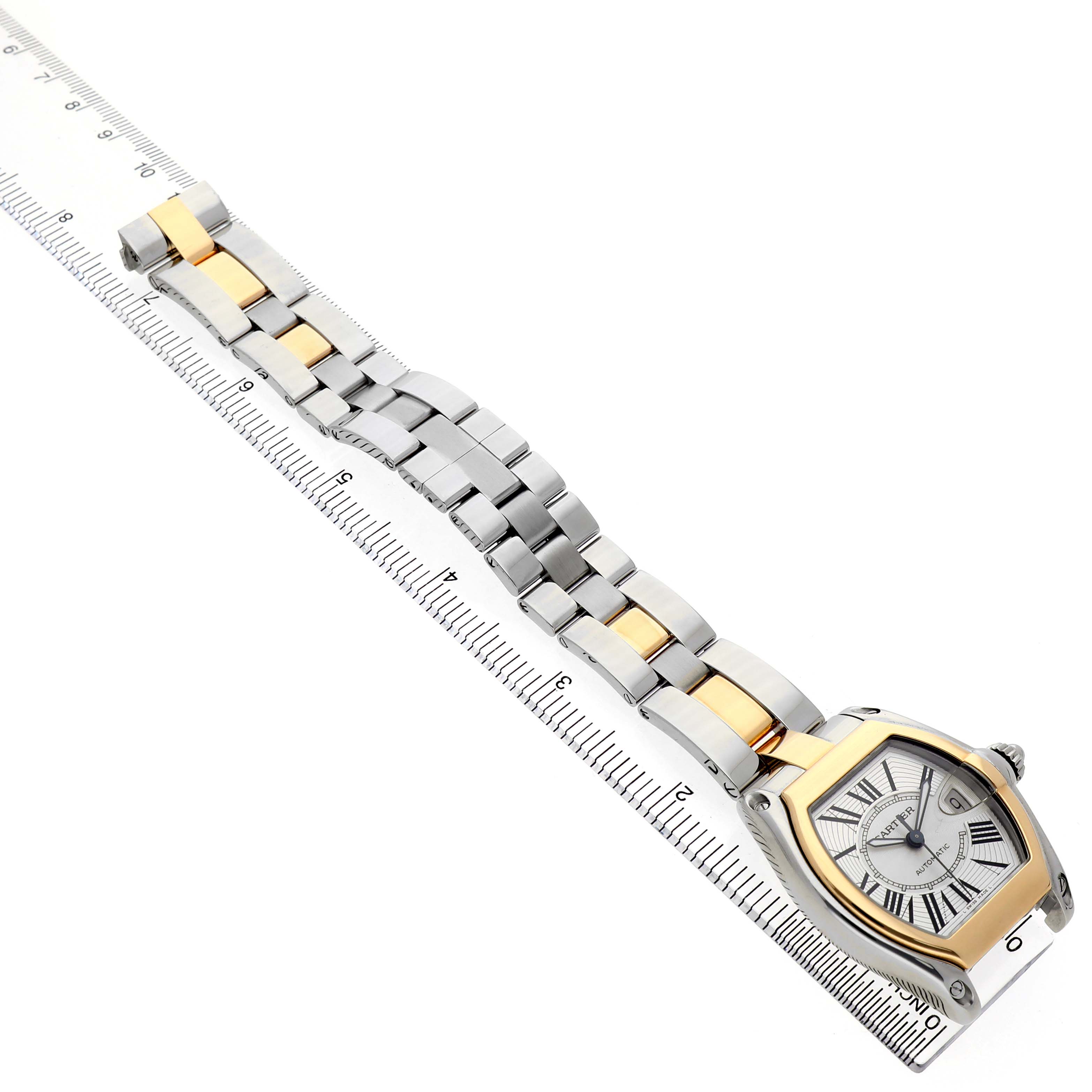 The Cartier Roadster W62031Y4 Men's Steel and Gold (two tone) Silver Dial watch is shown diagonally, highlighting its face, bracelet, and part of a ruler for scale.