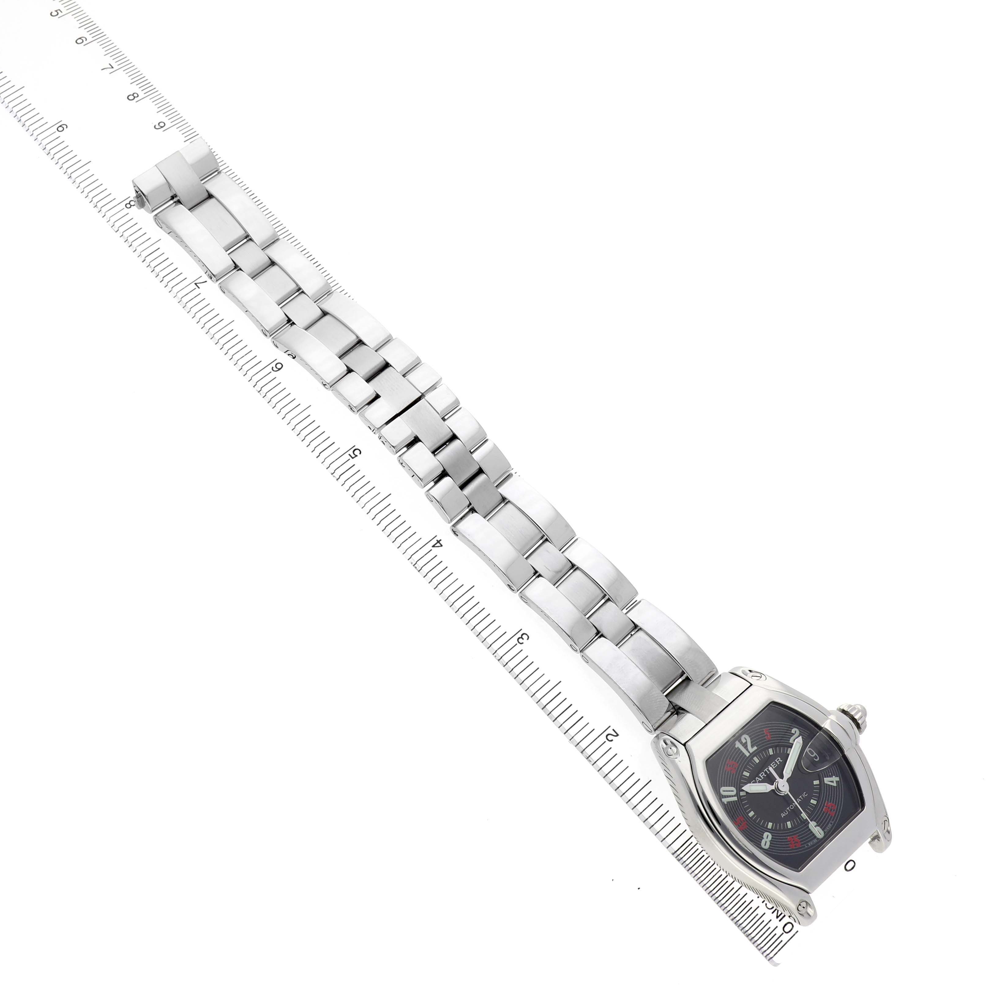 The Cartier Roadster W62002V3 Men's Stainless Steel Black Dial watch is shown from an overhead angle, displaying the full bracelet and face adjacent to a ruler.