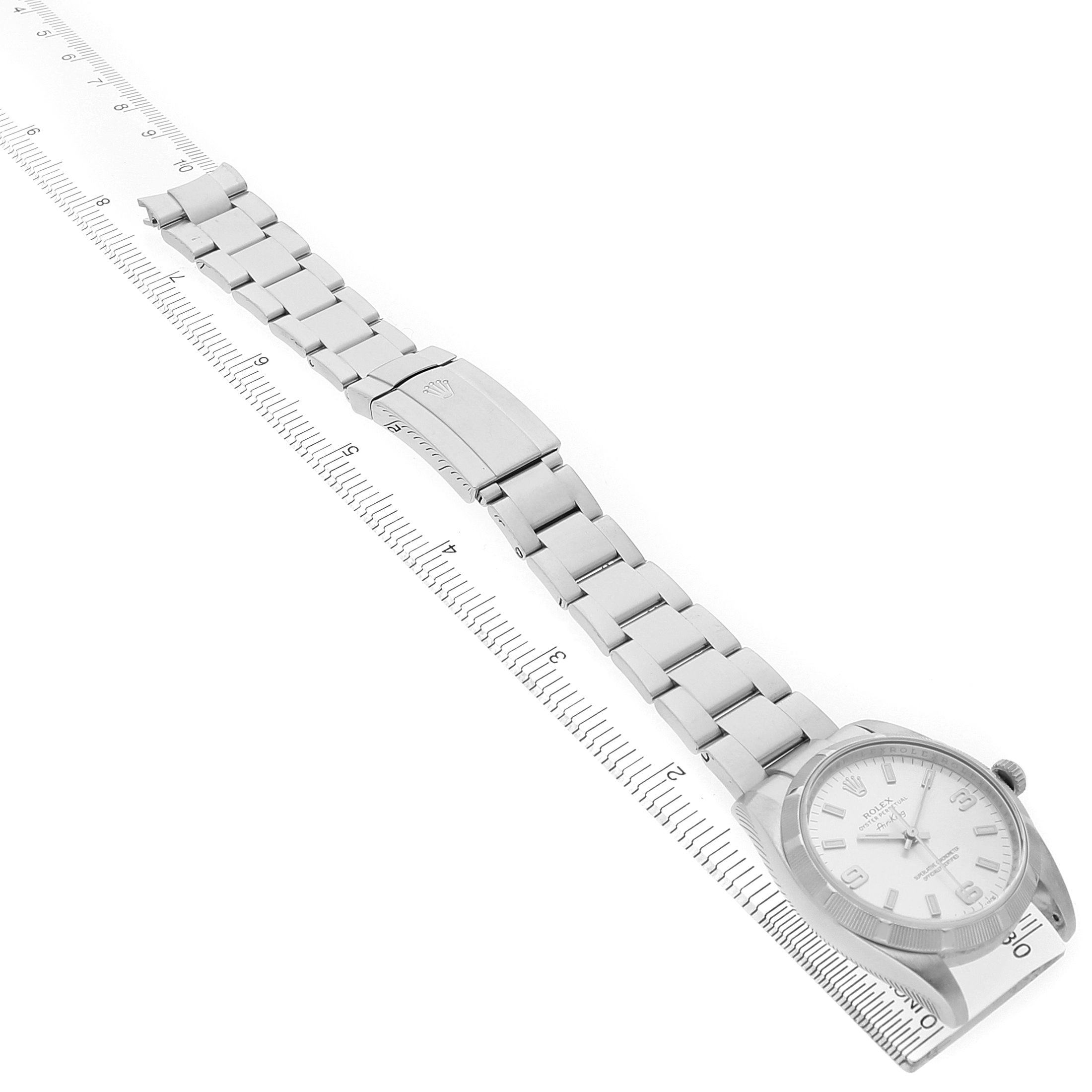The Rolex Air-King 114210 Men's Stainless Steel Silver Dial watch is shown from an angled top view, displaying the face, bracelet, and clasp alongside a ruler for scale.