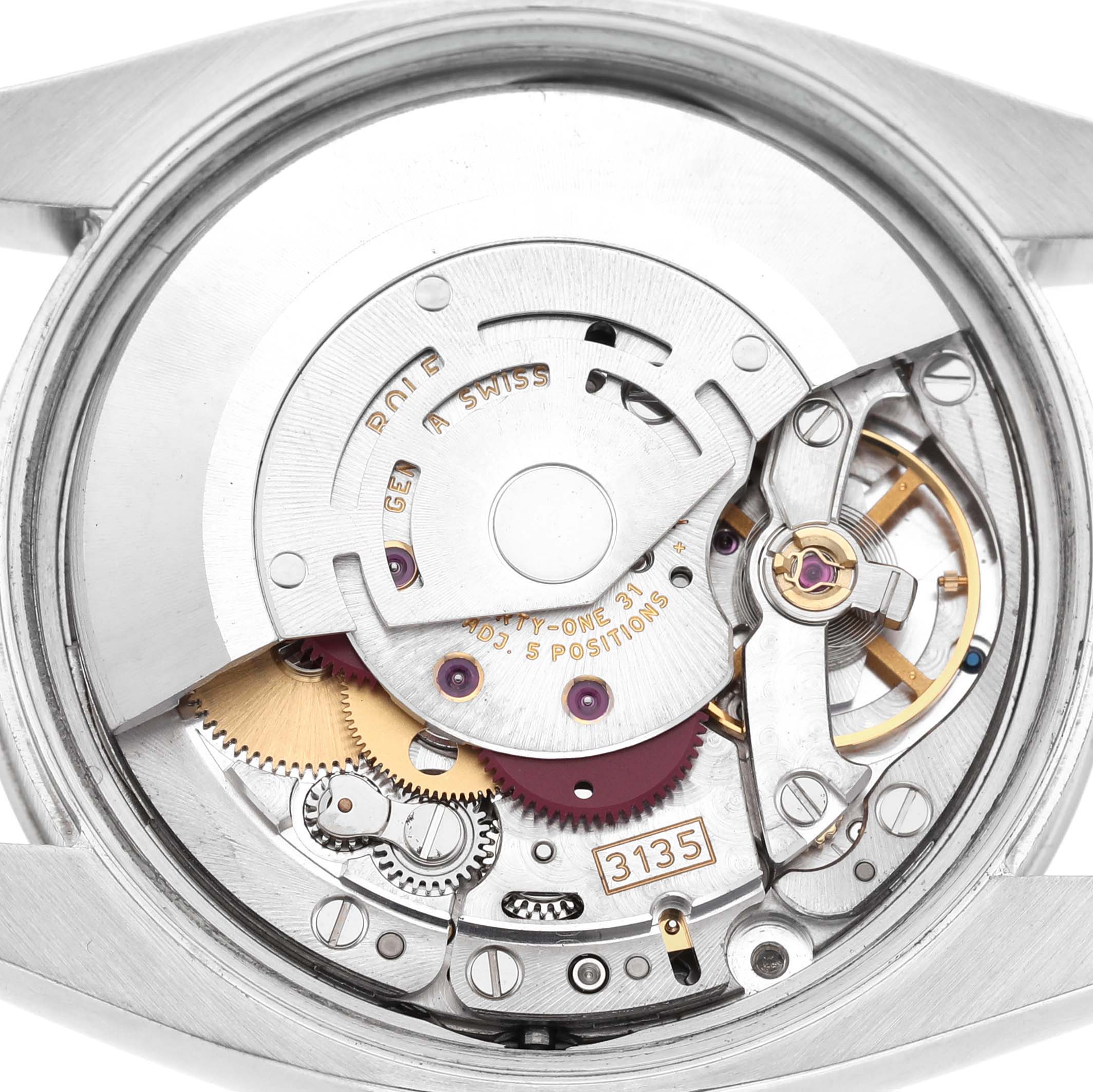 The image shows the movement of a Rolex Date 115200 Men's Stainless Steel White Dial model, highlighting internal components like gears and balance wheel viewed from the back.