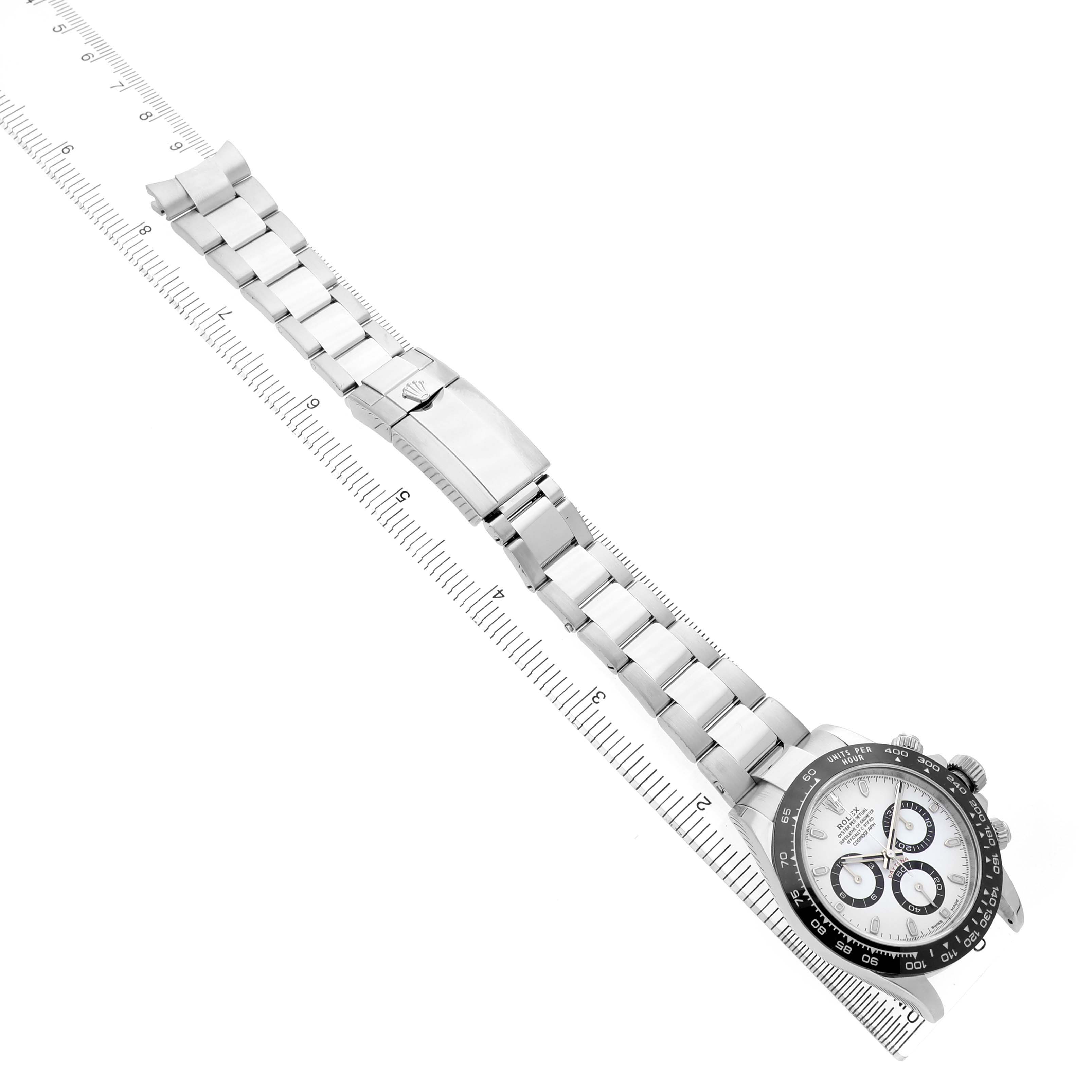 The Rolex Daytona 116500LN Men's Stainless Steel White Dial watch is shown from a diagonal top view, highlighting the bracelet and clasp next to a ruler.