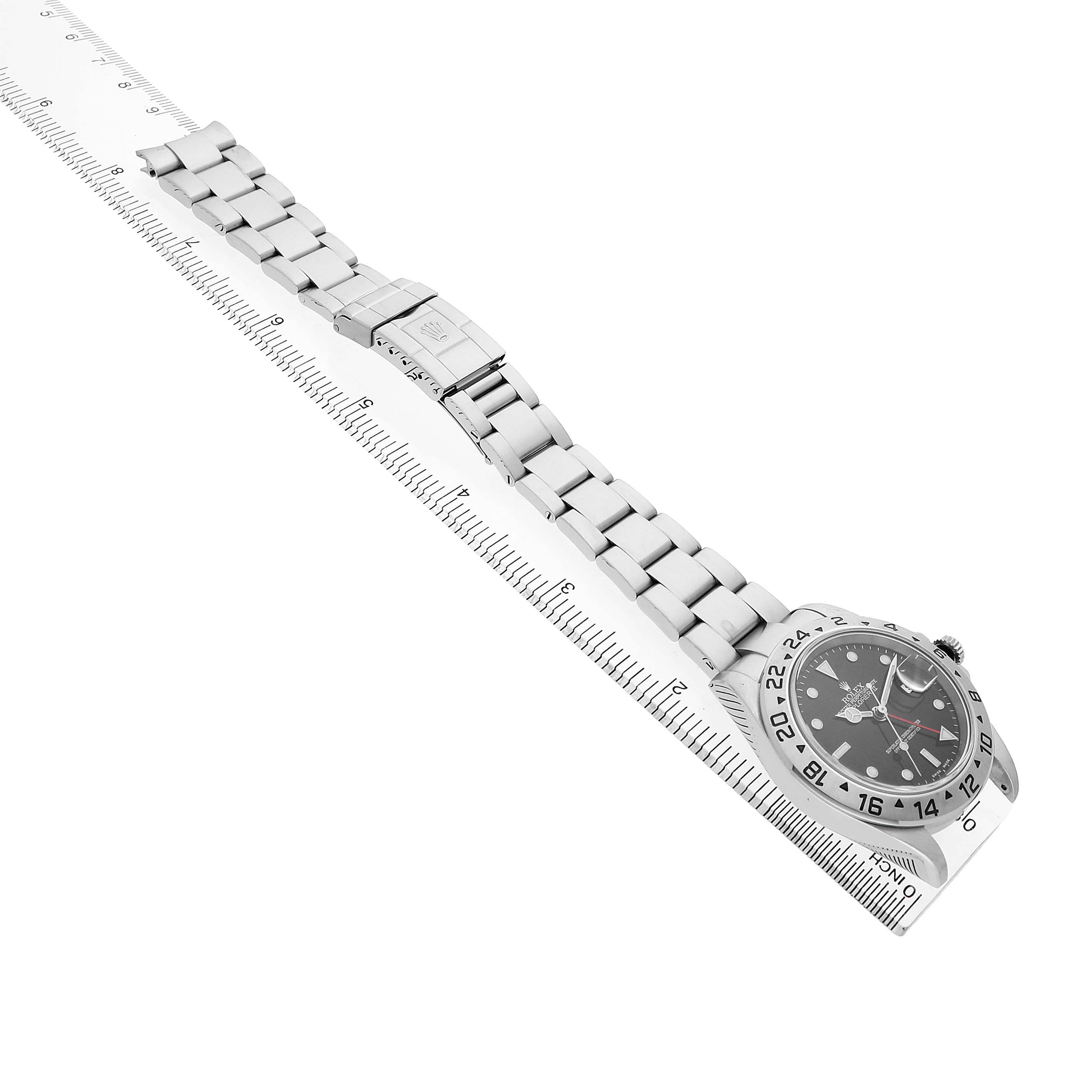 The Rolex Explorer 16570 T Men's Stainless Steel Black Dial watch is shown from a top angle, displaying the watch face, bezel, bracelet, and clasp on a ruler for scale.