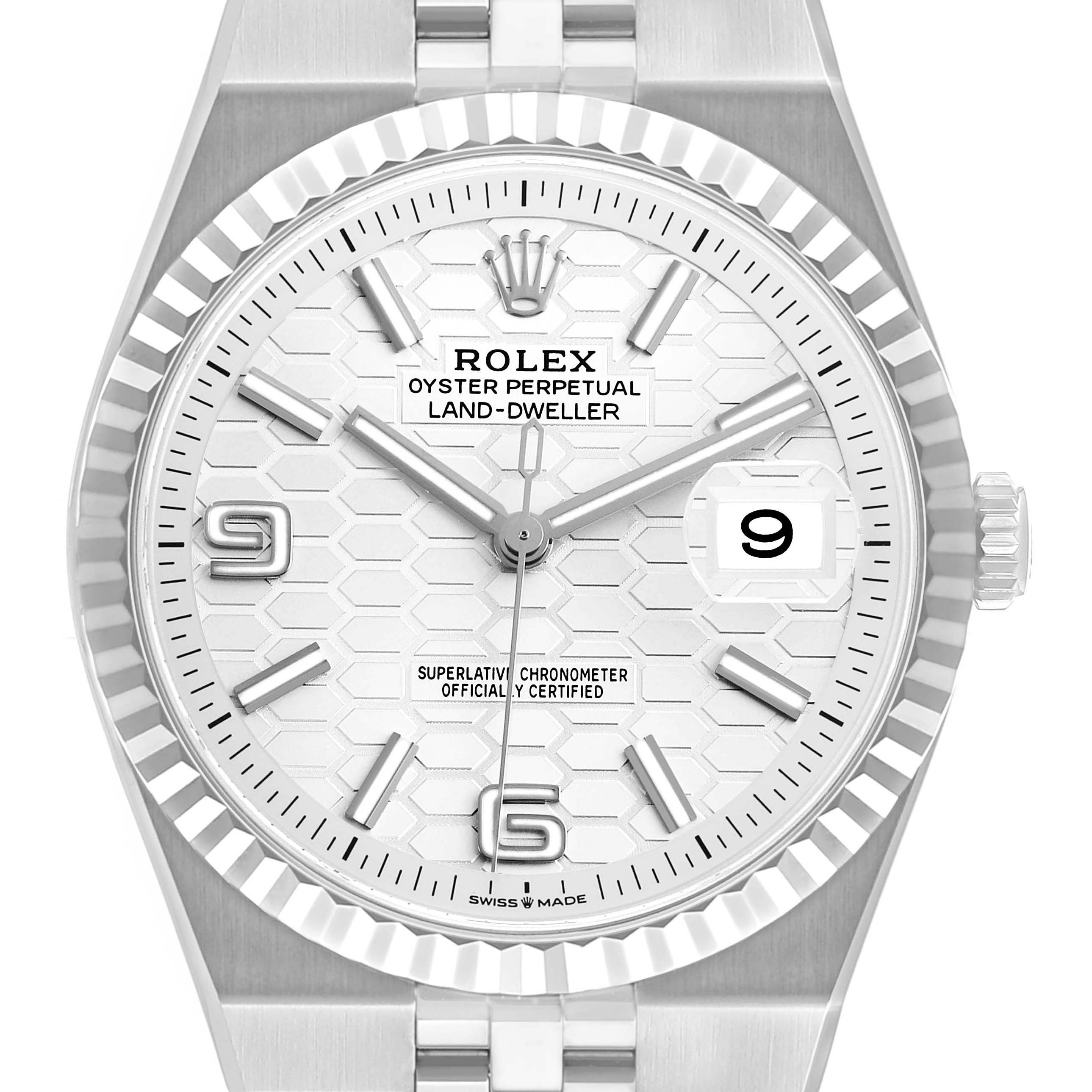 The Rolex Land-Dweller watch is shown from the front, highlighting the dial, fluted bezel, and date window.