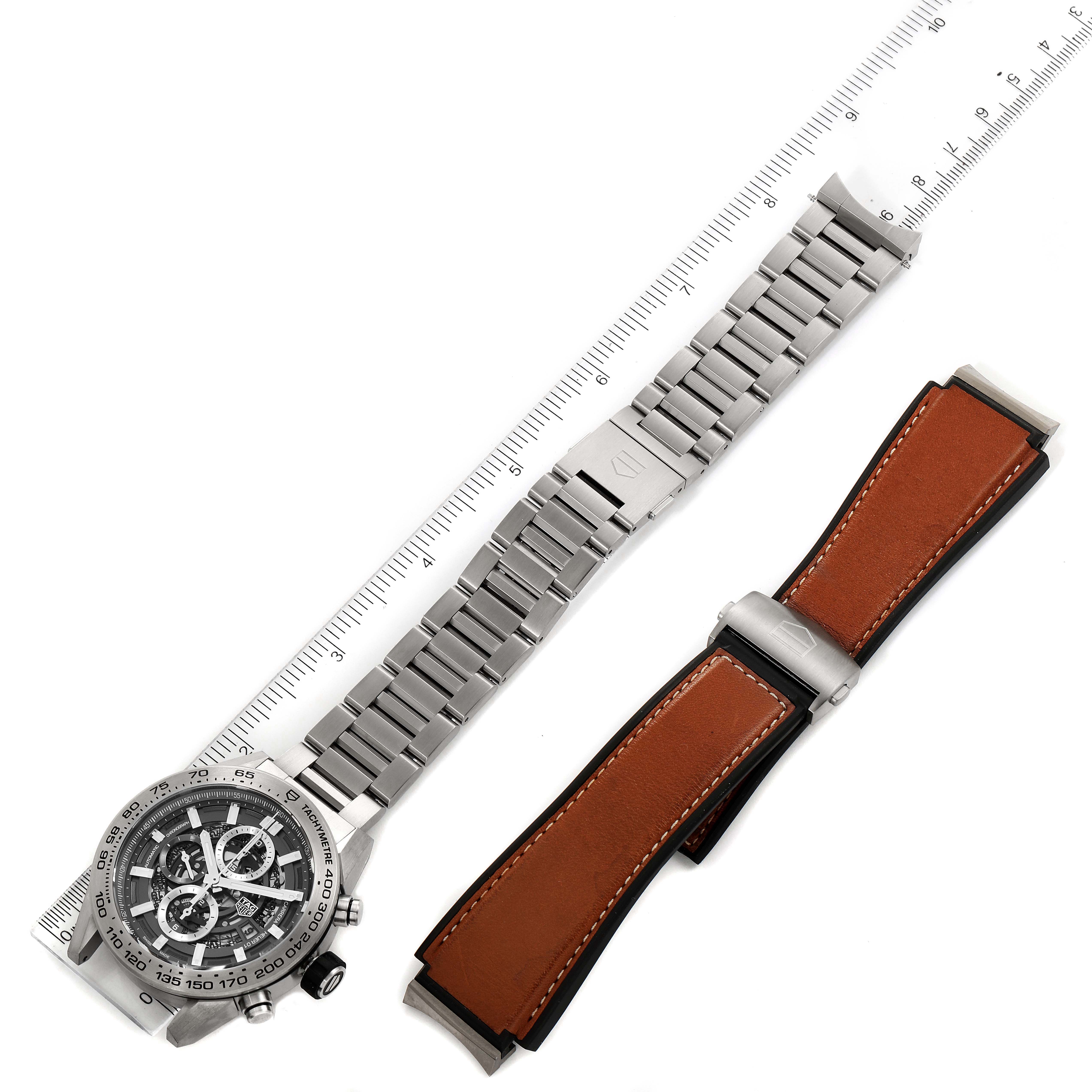 This image shows a top view of a Tag Heuer Carrera CAR2A8A.FT6072 Men's Titanium Grey Dial CAR2A8A.FT6072 Men's Titanium Grey Dial watch alongside an extra leather strap and a metal bracelet measured by a ruler.