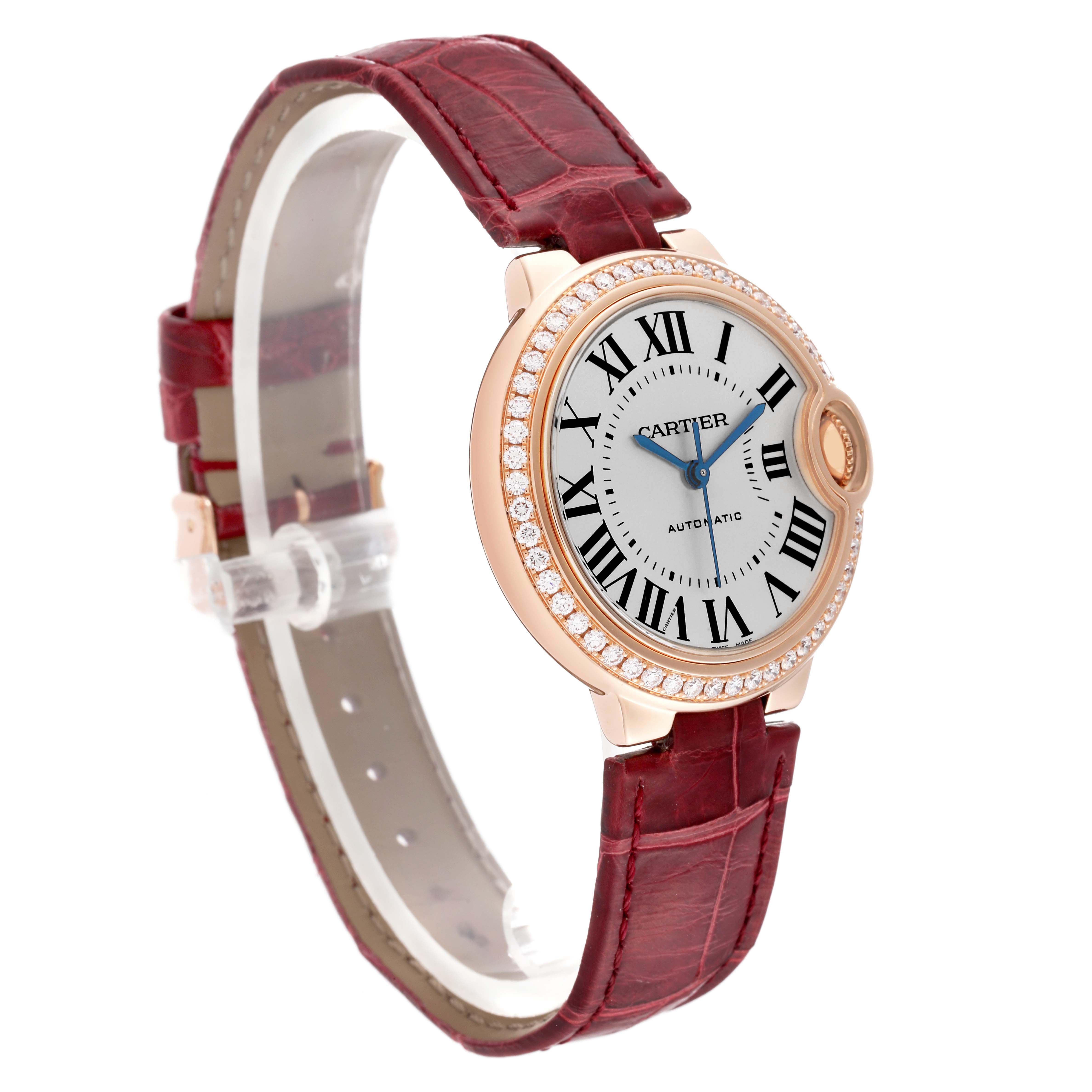 The Cartier Ballon Bleu WJBB0033 Women's Rose Gold Silver Dial watch is shown at a three-quarter angle, highlighting the diamond bezel, dial, and red leather strap.