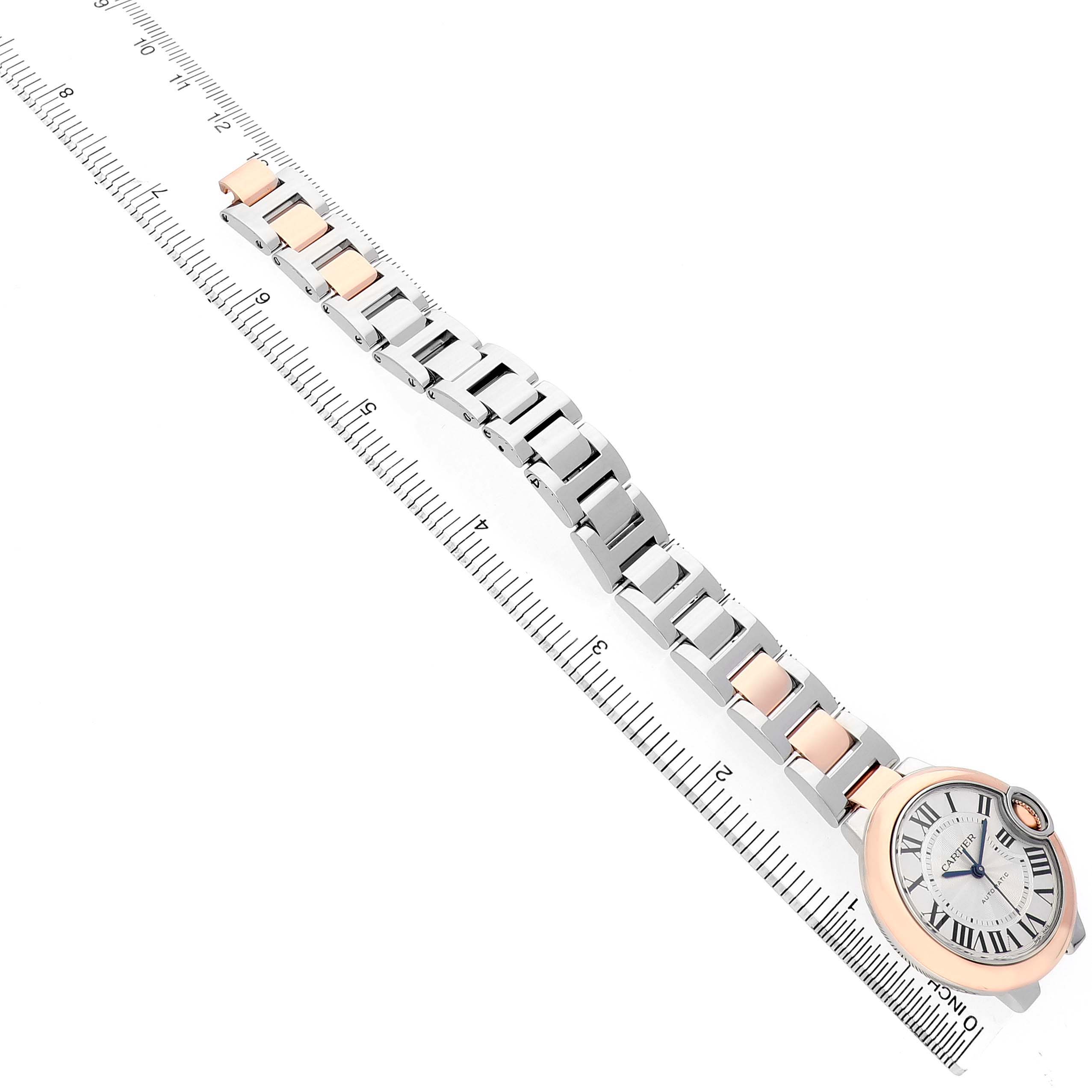 The image shows the Ballon Bleu by Cartier at an angled top view, focusing on the watch face and metal bracelet beside a ruler.