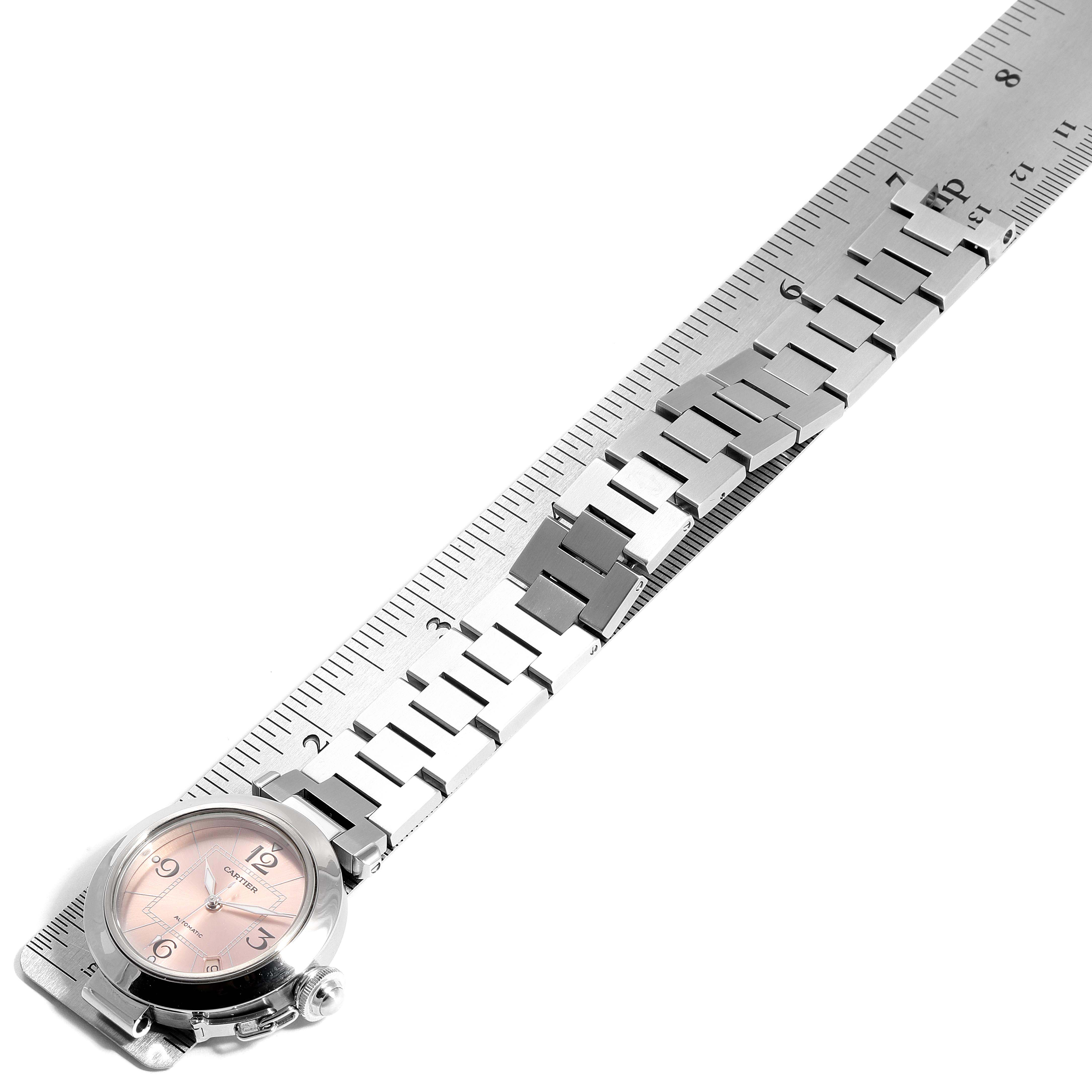The image shows a top-down view of a Cartier Pasha W31075M7 Women's Stainless Steel Pink Dial W31075M7 Women's Stainless Steel Pink Dial watch, highlighting its face and metal bracelet alongside a metal ruler.