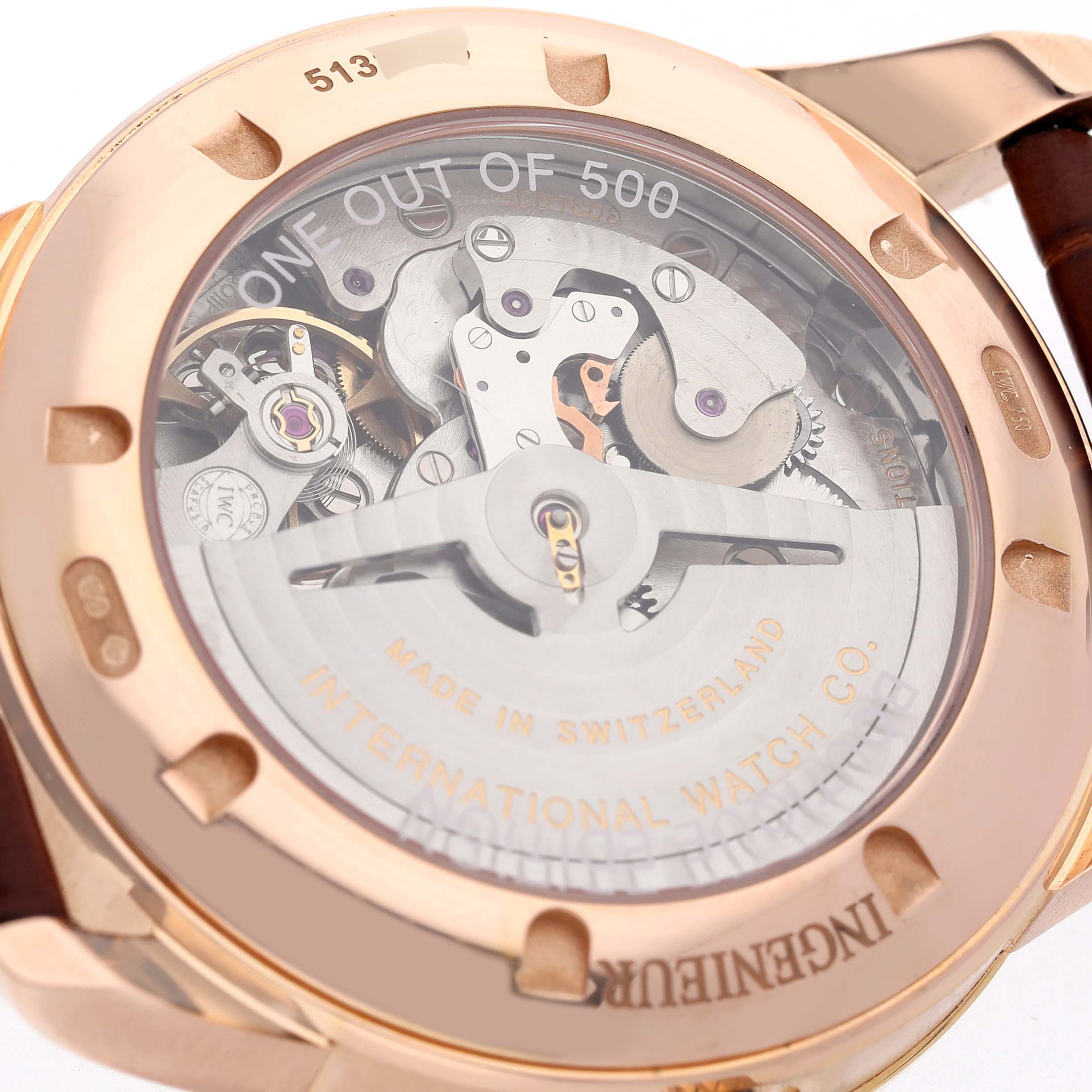 The image shows the back of the IWC Ingenieur IW323312 Men's Rose Gold Brown Dial watch, revealing its internal mechanical movement through a transparent case back.