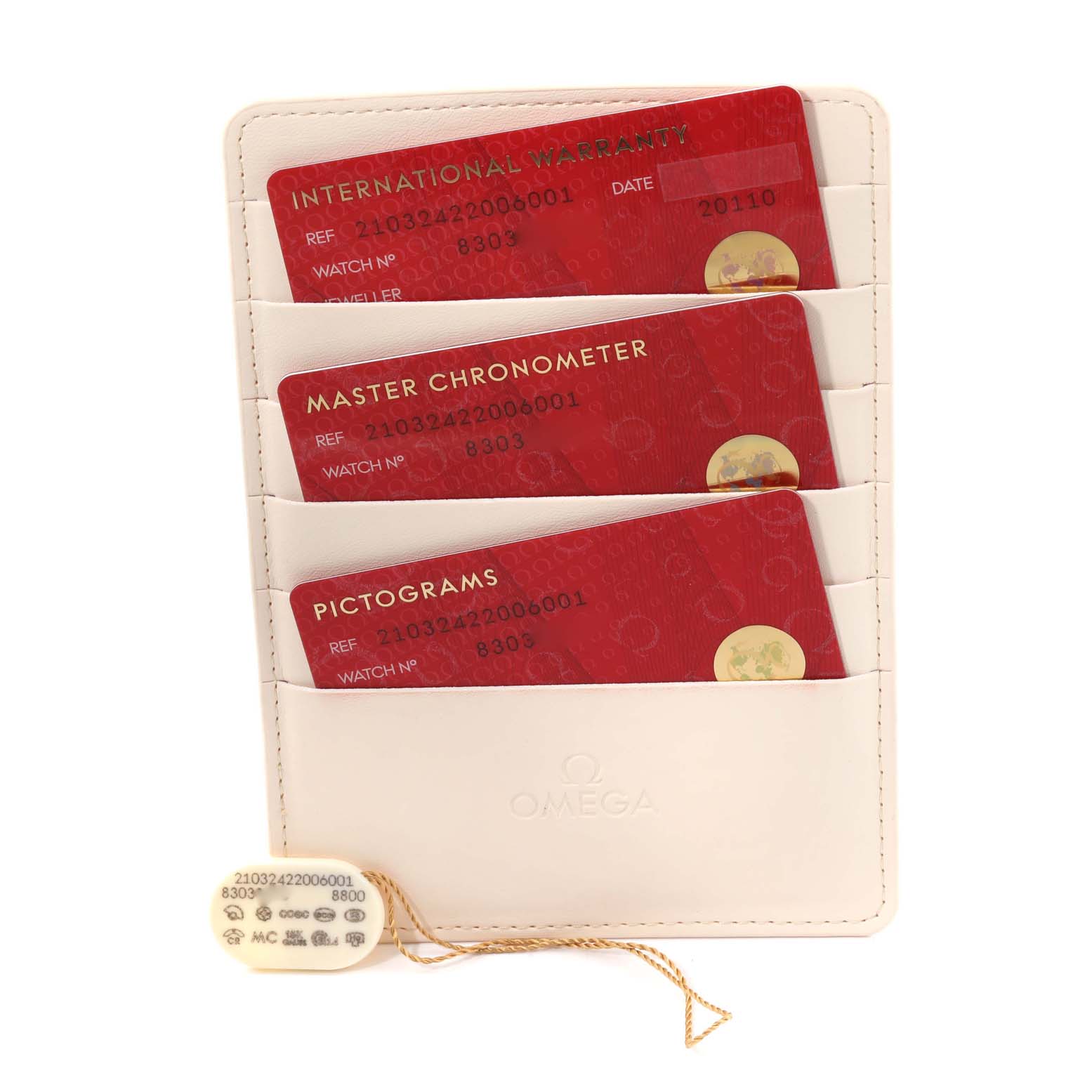 The image shows three red cards labeled "International Warranty," "Master Chronometer," and "Pictograms," along with a hanging tag in an Omega holder.