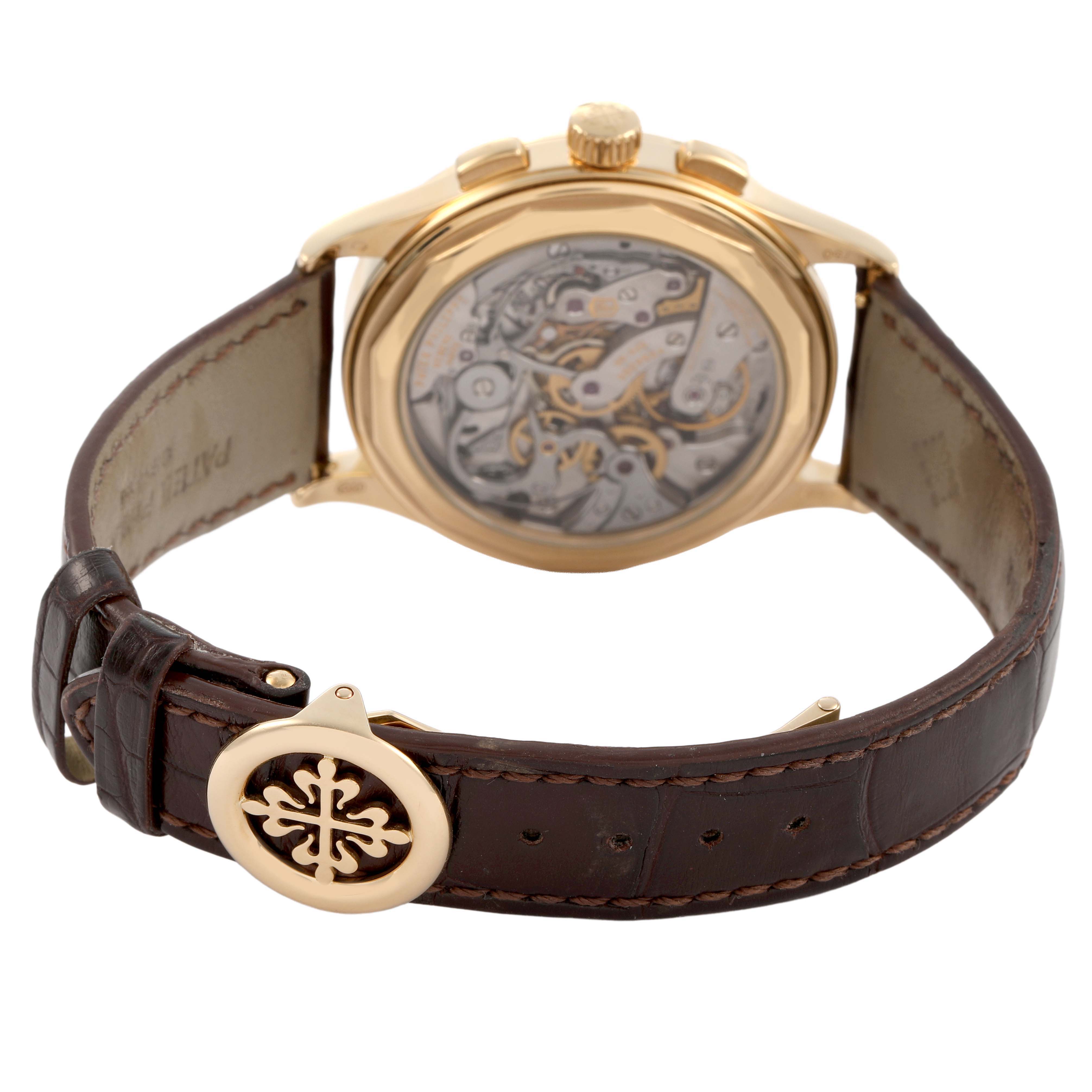 The Patek Philippe Complications 5170J-001 Men's Yellow Gold Silver Dial watch is shown from the back, revealing the movement and a leather strap with the buckle logo.