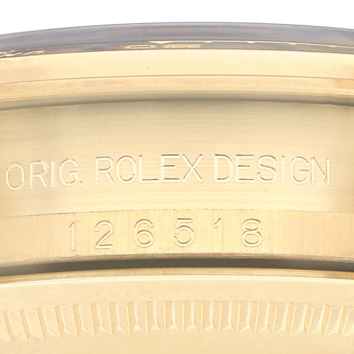 The image shows a close-up of the side engraving on a Rolex Daytona 126518 Men
s Yellow Gold White Dial 126518 Men
s Yellow Gold White Dial watch, featuring the words "ORIG. ROLEX DESIGN" and model number.