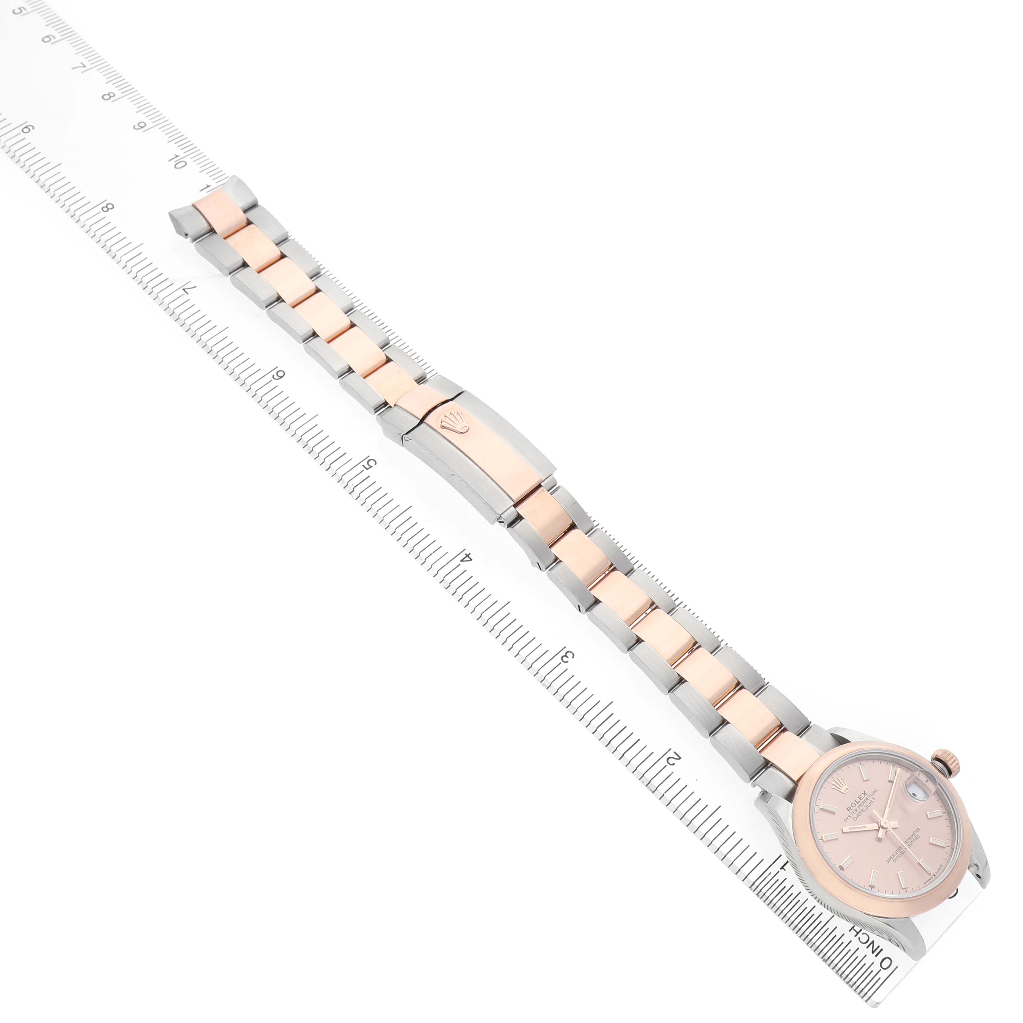 The Rolex Datejust 278241-0009 Women's Steel and Gold (two tone) Pink Dial watch is shown at an angled top view, displaying the full bracelet, clasp, and face next to a ruler.