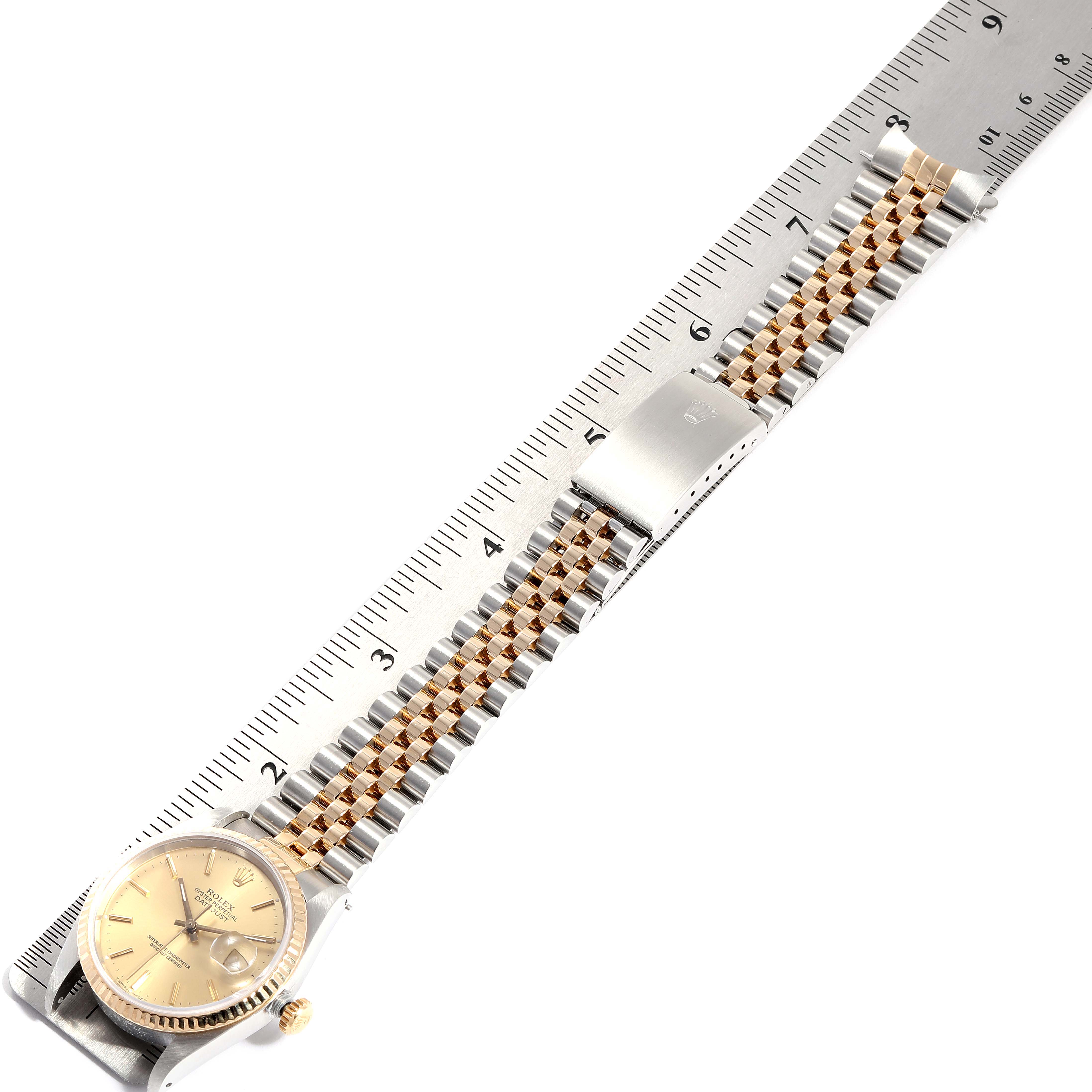The Rolex Datejust 16233 Men
s Steel and Gold (two tone) Champagne Dial 16233 Men
s Steel and Gold (two tone) Champagne Dial watch is shown from a top-down angle with the bracelet and clasp fully extended next to a ruler.