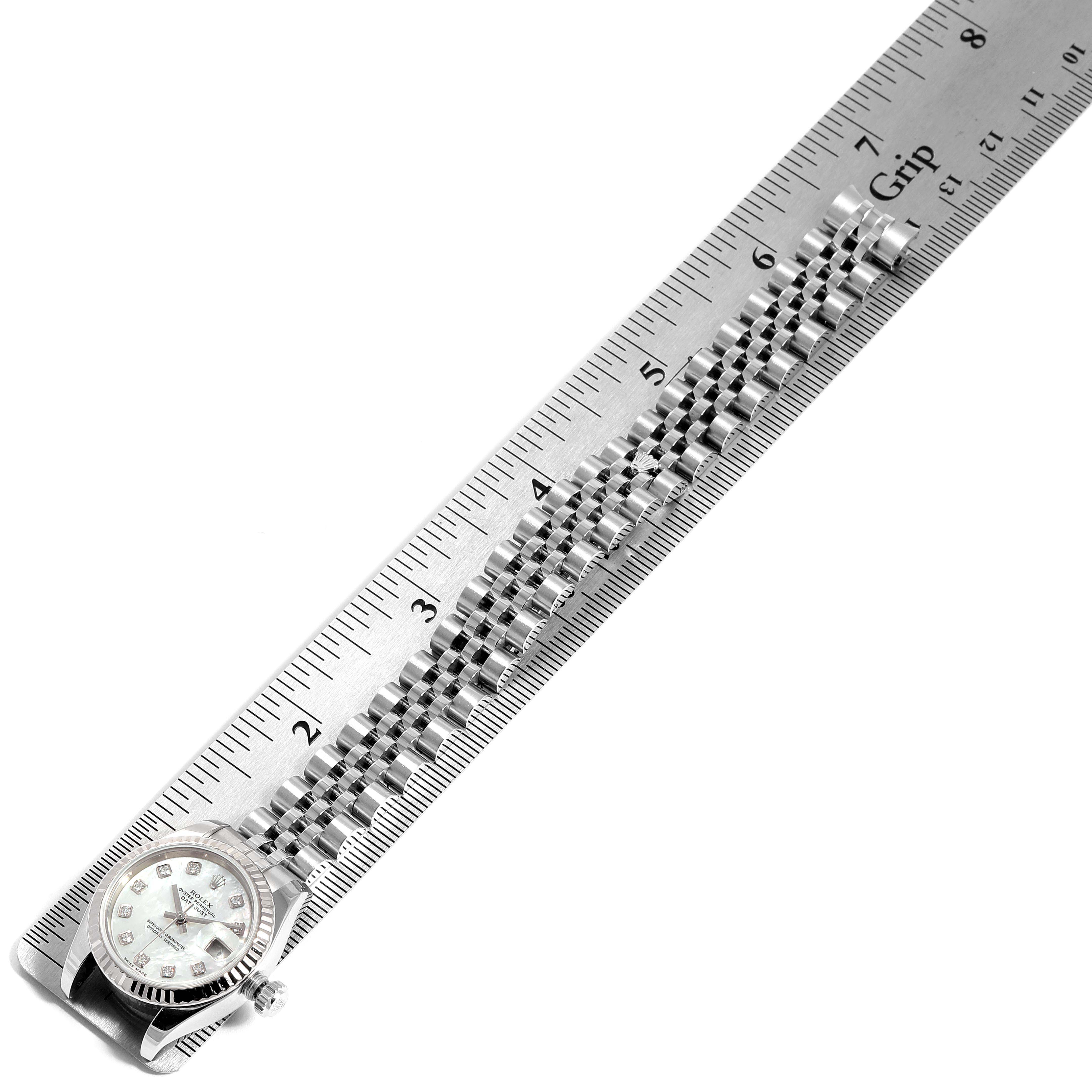The image shows the Rolex Datejust 179174 Women's Stainless Steel Mother of Pearl Dial 179174 Women's Stainless Steel Mother of Pearl Dial watch laid beside a ruler, highlighting the band and watch face.