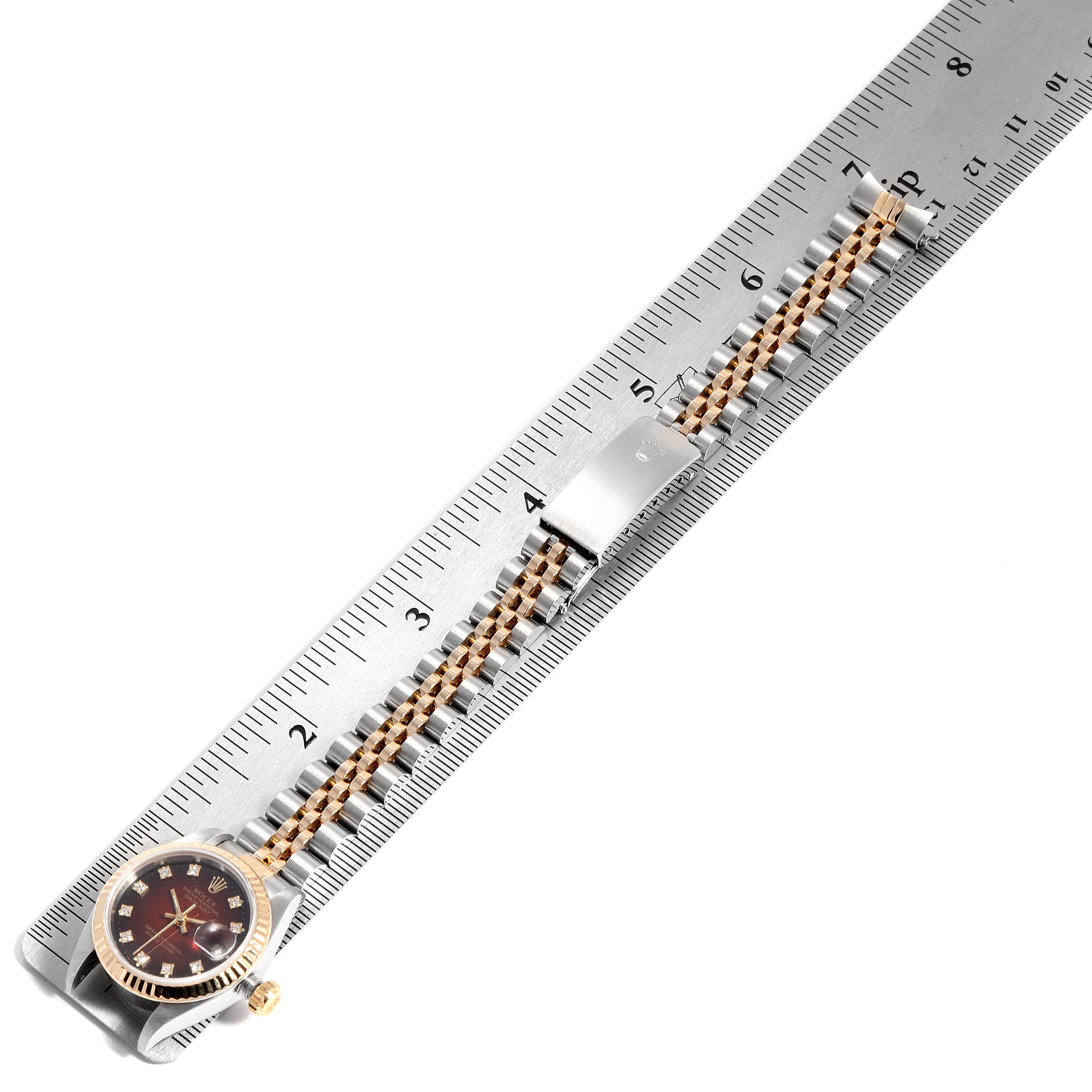 The image shows a Rolex Datejust 69173 Women's Steel and Gold (two tone) Red Dial 69173 Women's Steel and Gold (two tone) Red Dial watch laid parallel to a ruler, displaying the face, crown, and metal bracelet with a clasp.