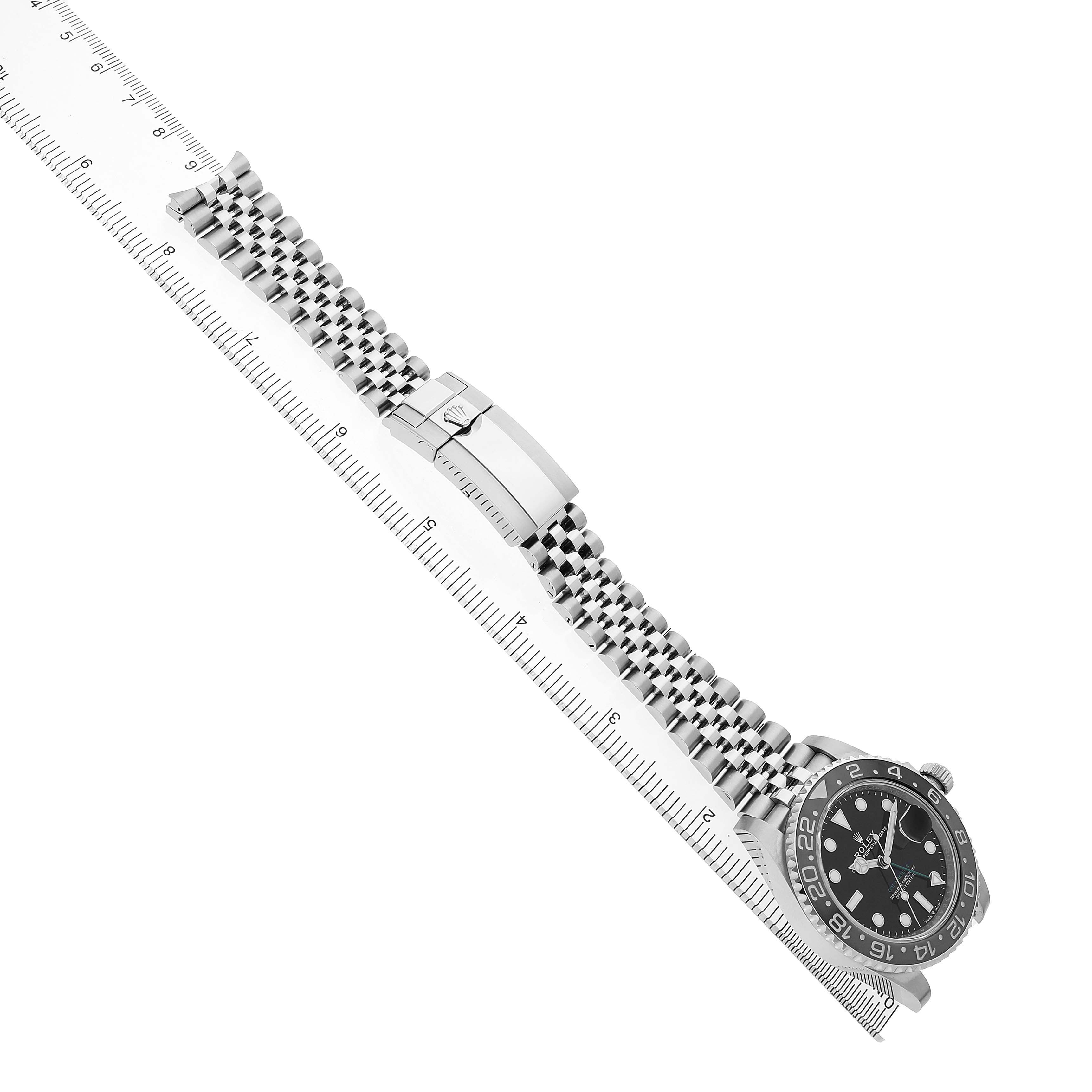 The Rolex GMT-Master M126710GRNR Men's Stainless Steel Black Dial watch is shown at an angled view, displaying its face, bezel, bracelet, and clasp alongside a ruler for scale.